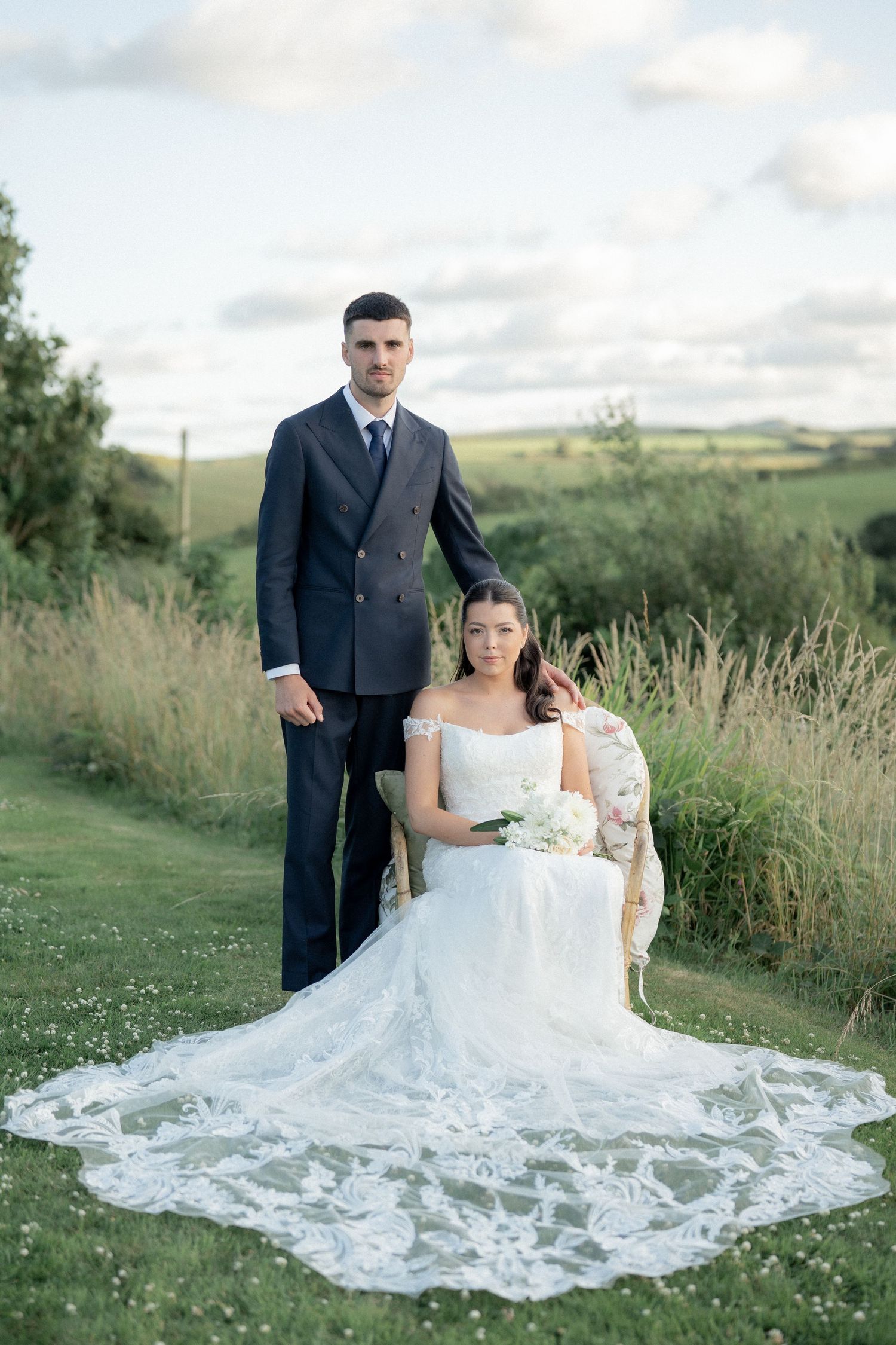 A wedding portrait of a couple in formal attire against a scenic countryside backdrop.