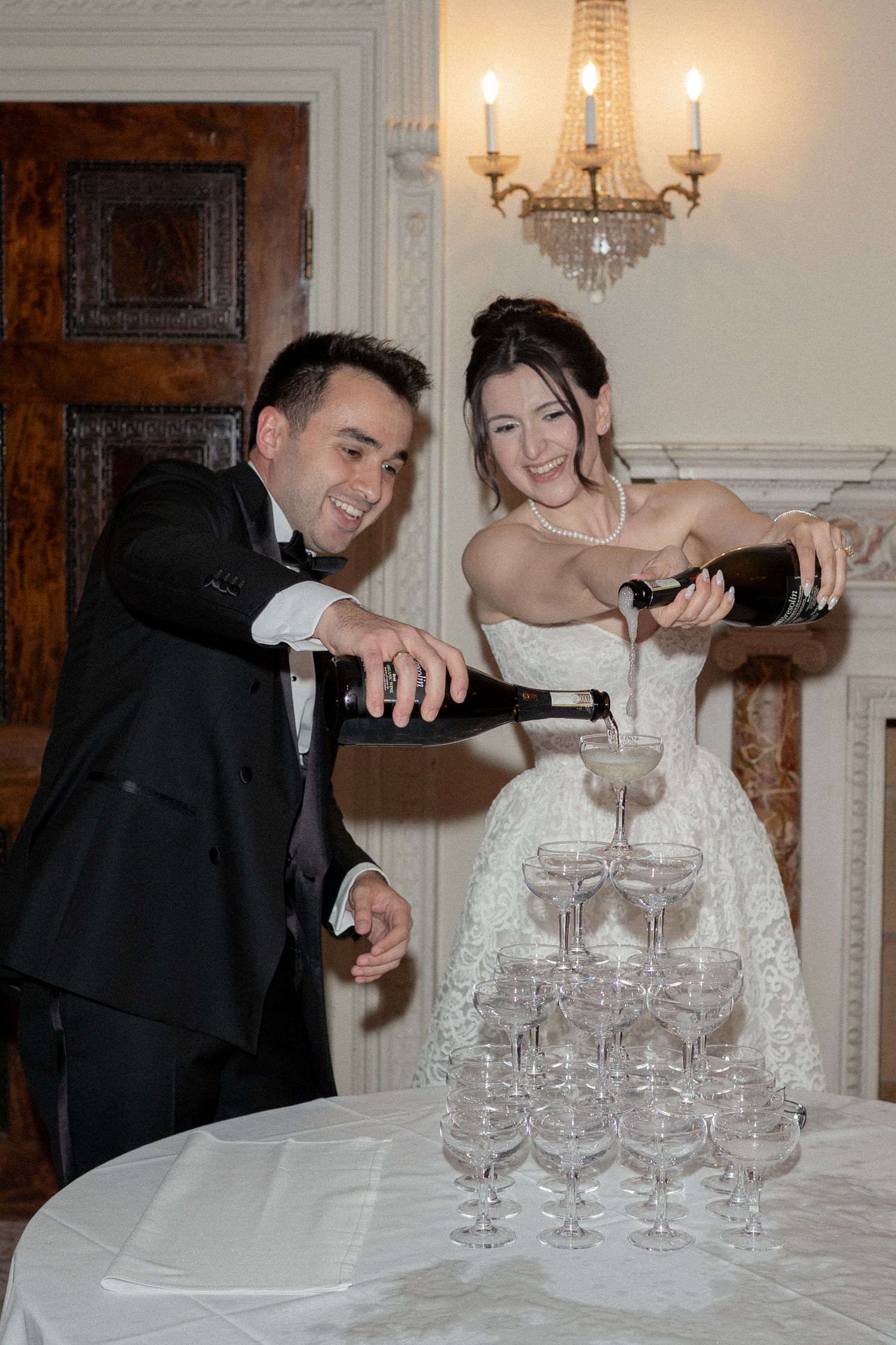 Couple pouring champagne into tower of glasses at elegant wedding reception.
