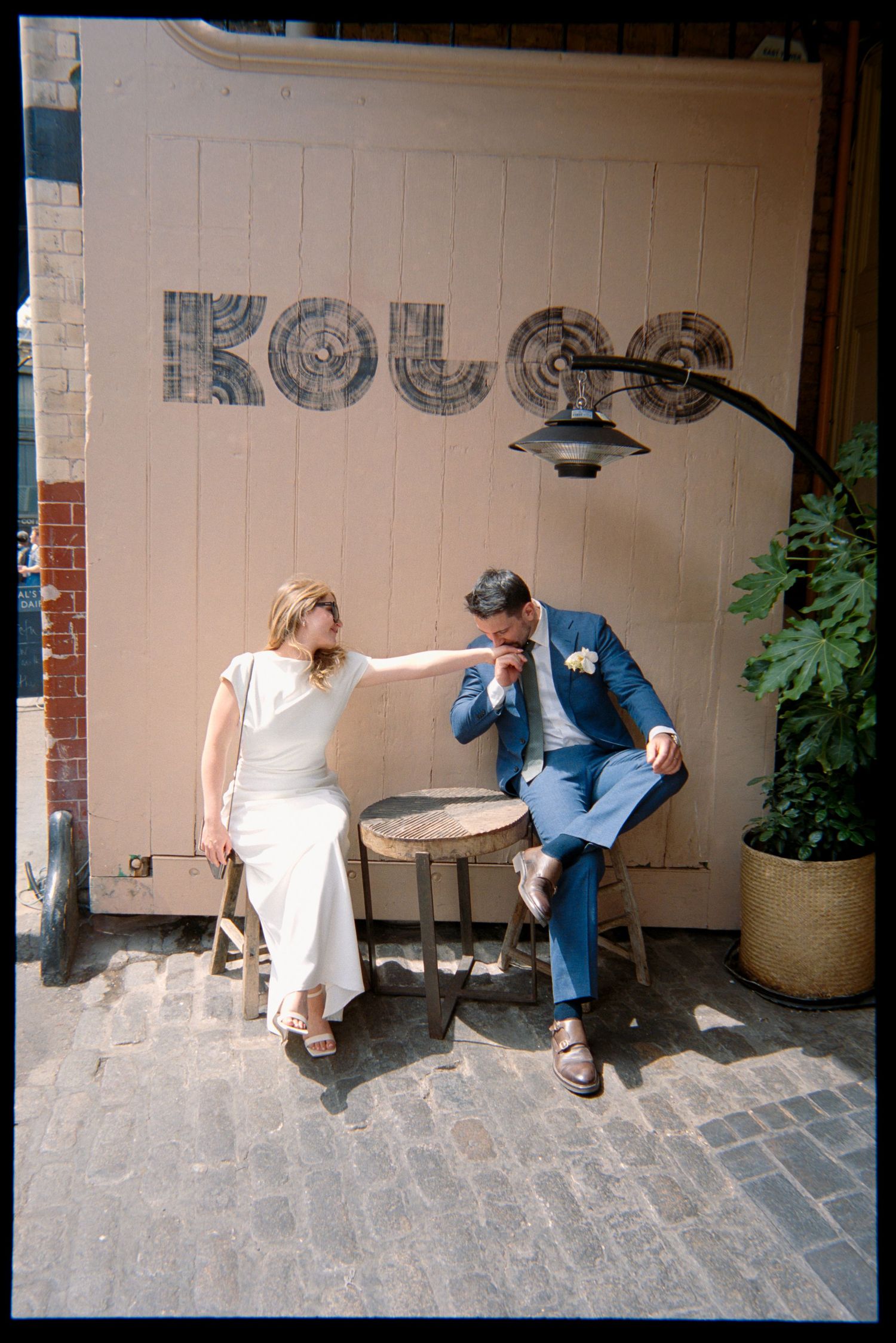 Bride and groom sitting outside Kolgo restaurant on cobblestone street, sharing an intimate moment in wedding attire.