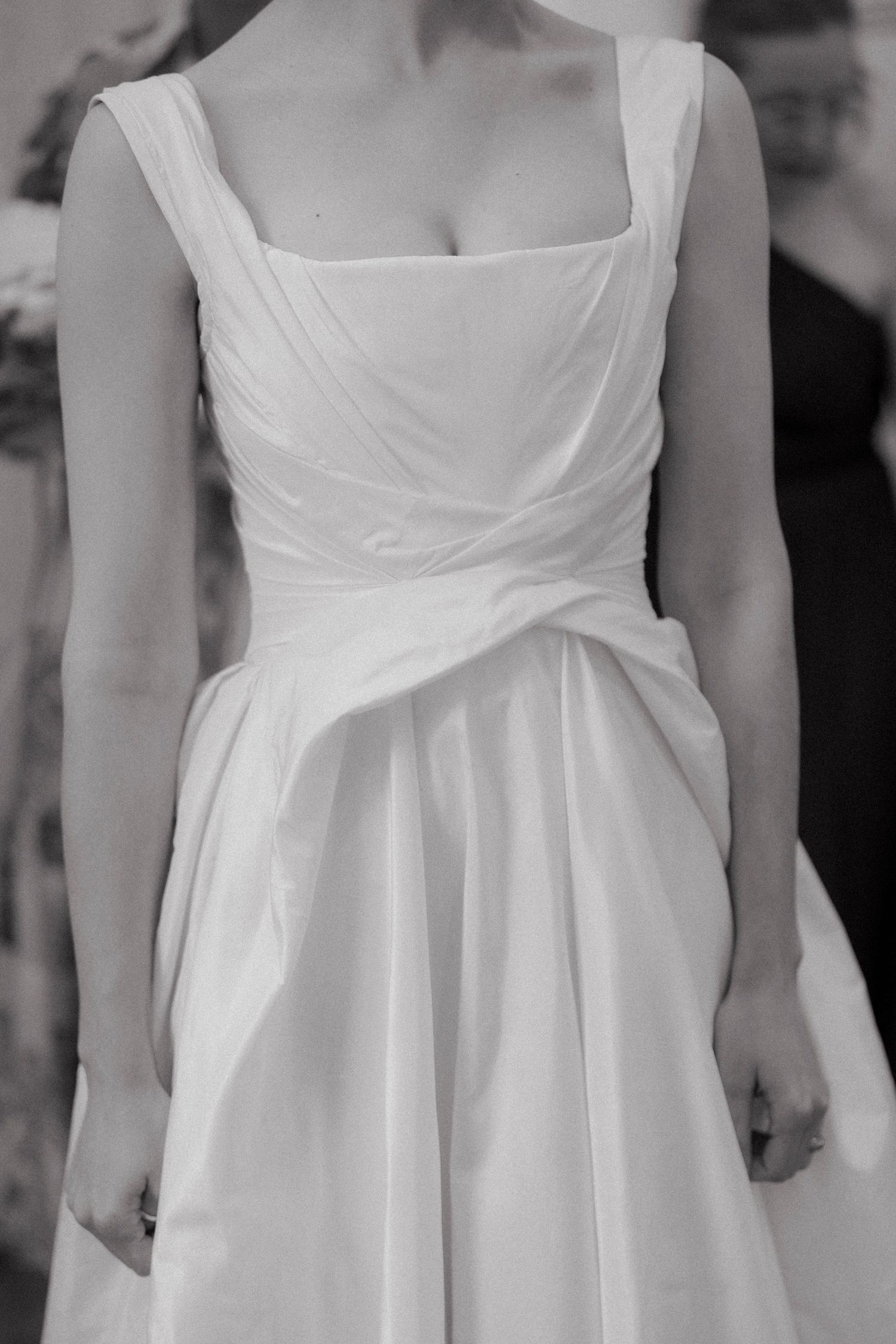 Black and white close-up of a bride wearing an elegant white wedding dress with a square neckline and draped wrap bodice.