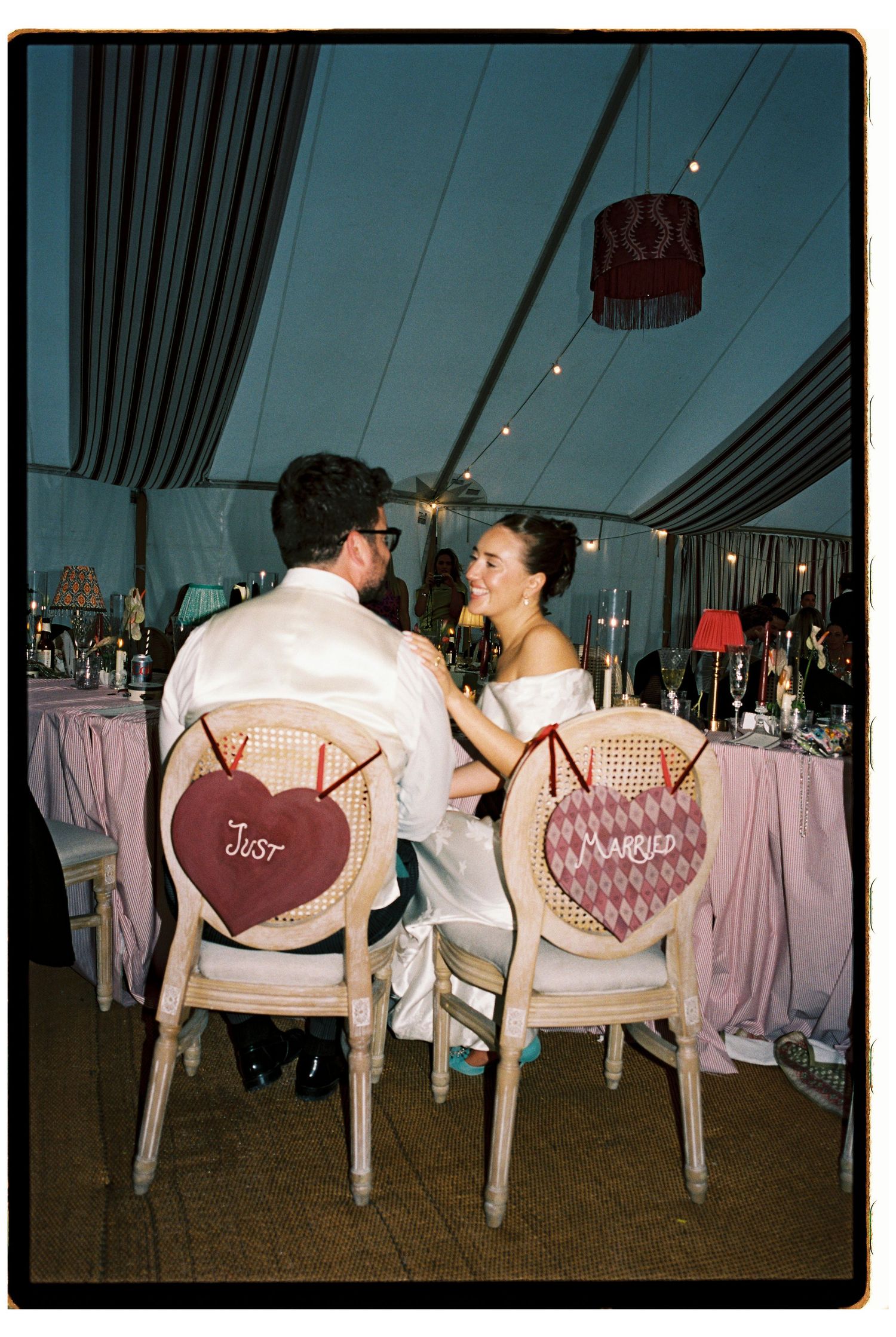 Newlyweds sit in decorated Just Married chairs at their elegant marquee wedding reception dinner.