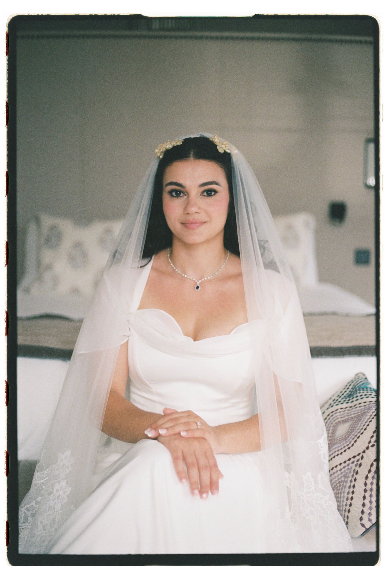 Bride in white gown and veil with floral headpiece sits elegantly before her wedding ceremony.