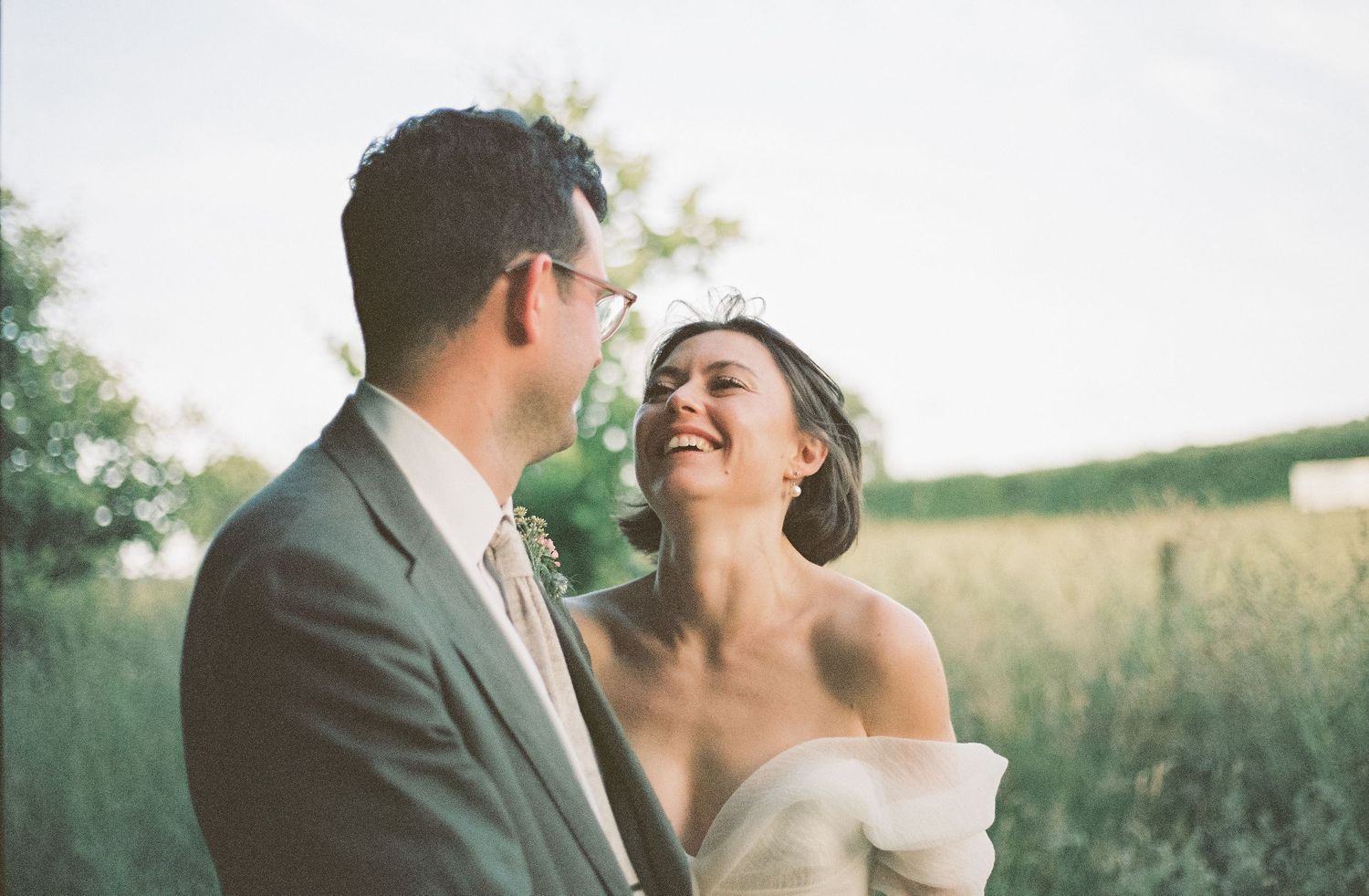 A romantic wedding couple embraces outdoors in a natural setting with soft lighting and bokeh effects.