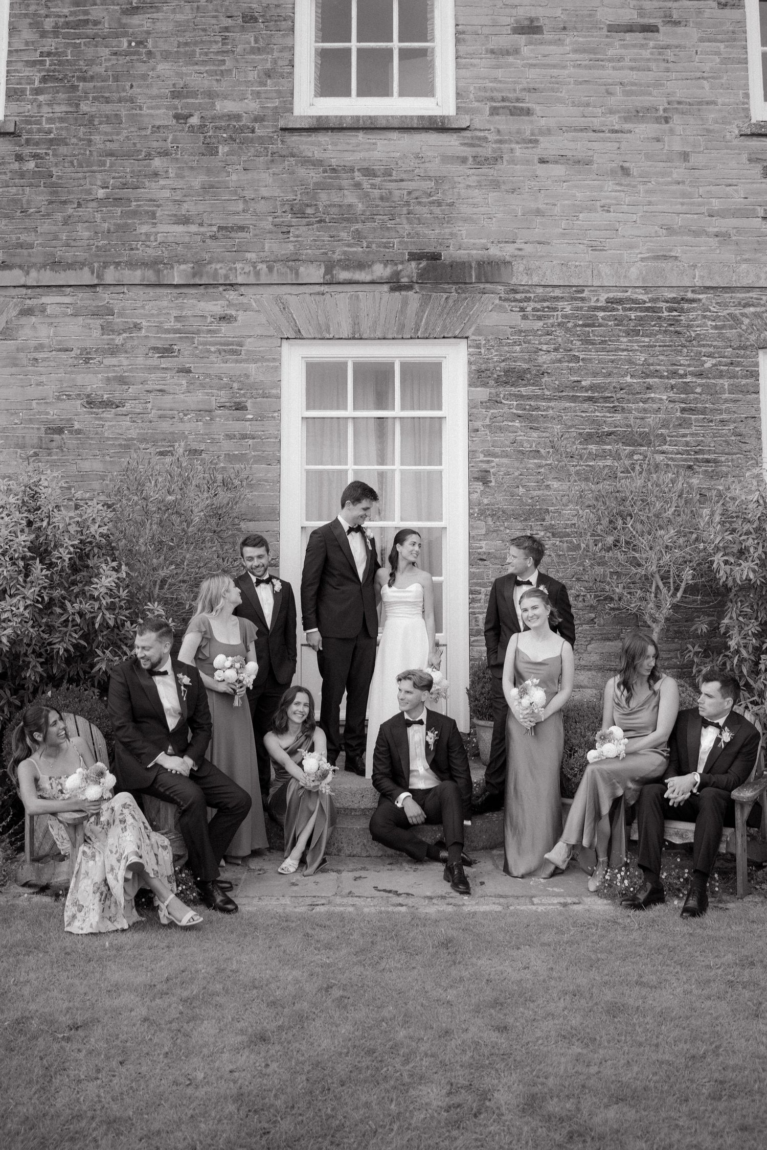 Black and white photo of a wedding party posed together in front of a brick building with white windows.