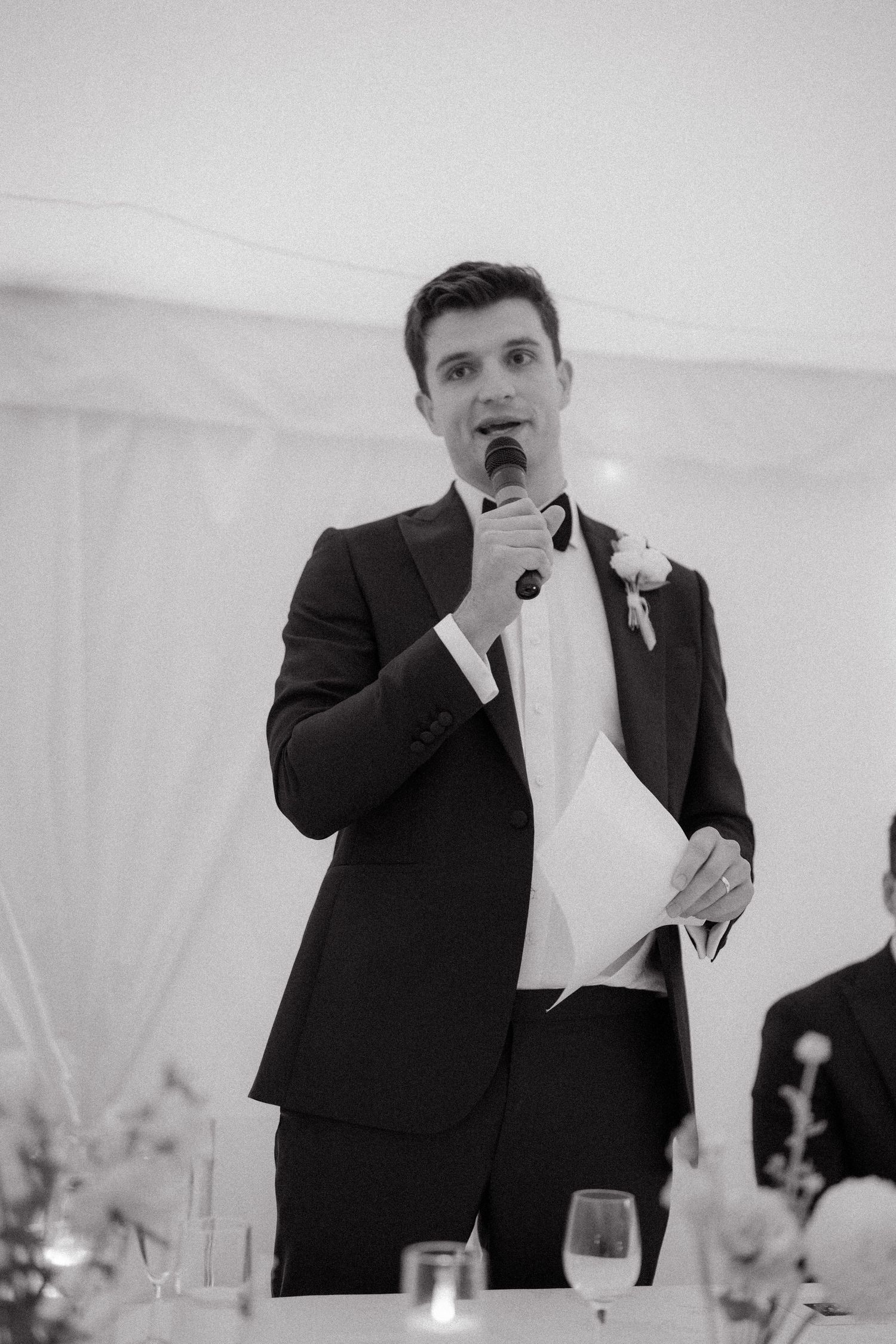 A speaker in formal attire gives a toast at a wedding reception.