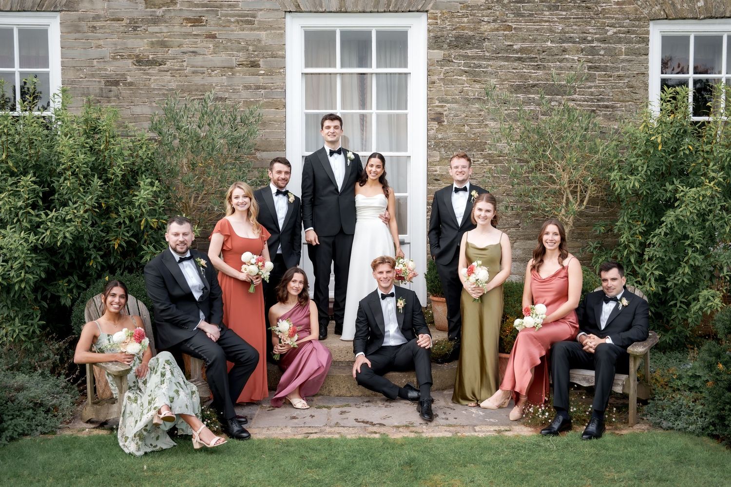 Wedding party members pose together on stone steps in formal attire for outdoor group photos.