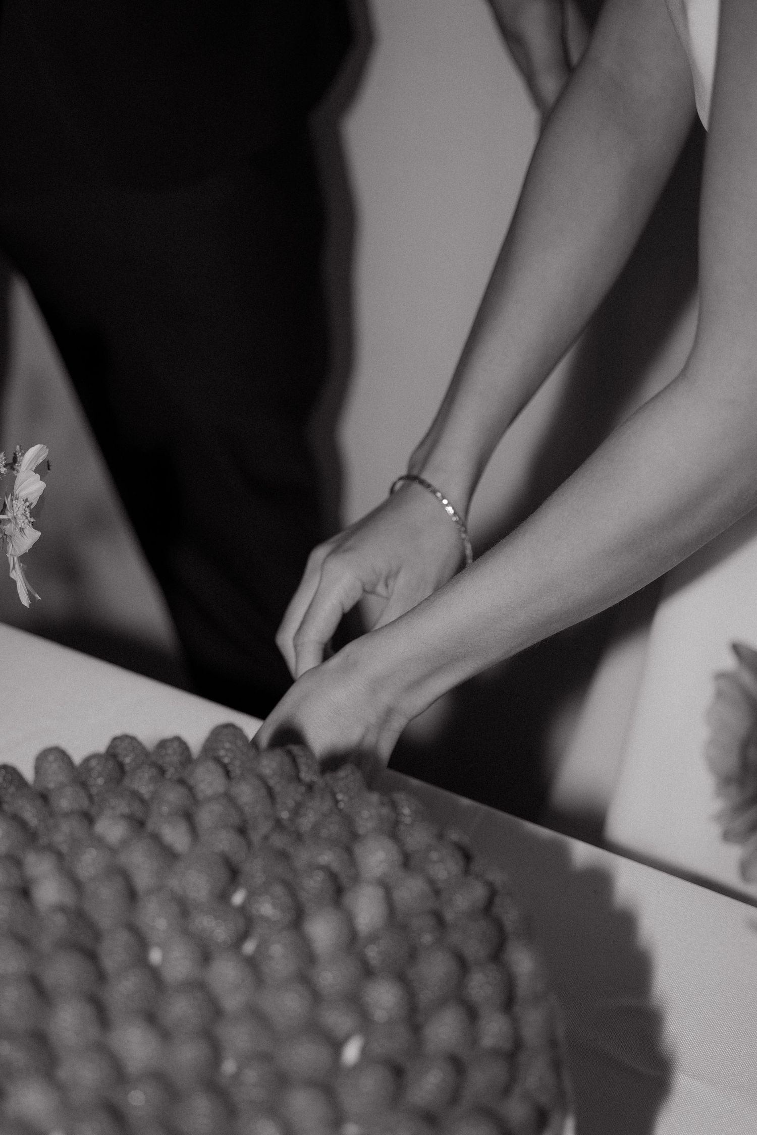Black and white close-up of hands rolling small spherical objects in a repetitive motion across a surface.