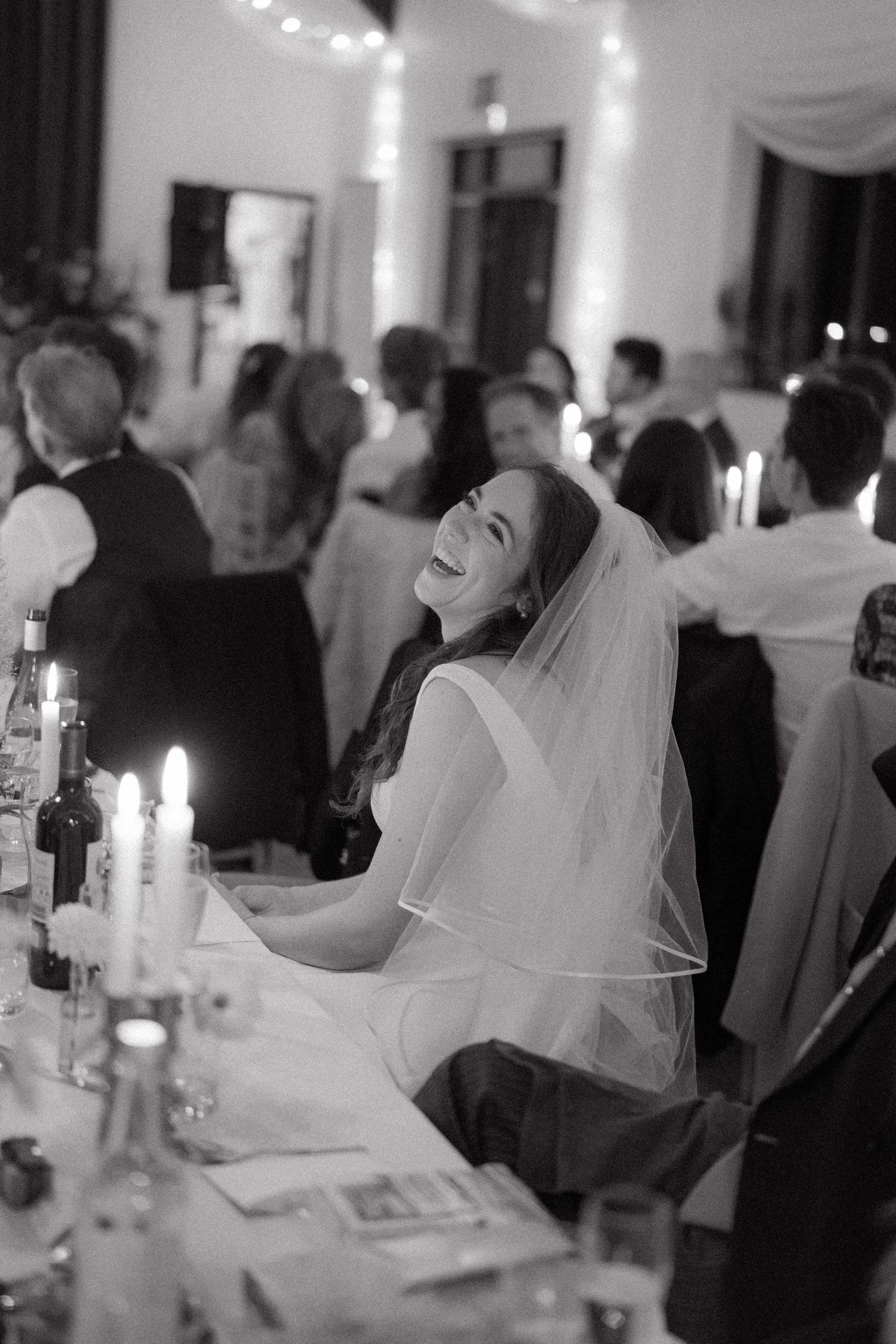 A black and white photo series showing a bride laughing joyfully during a candlelit wedding reception celebration.