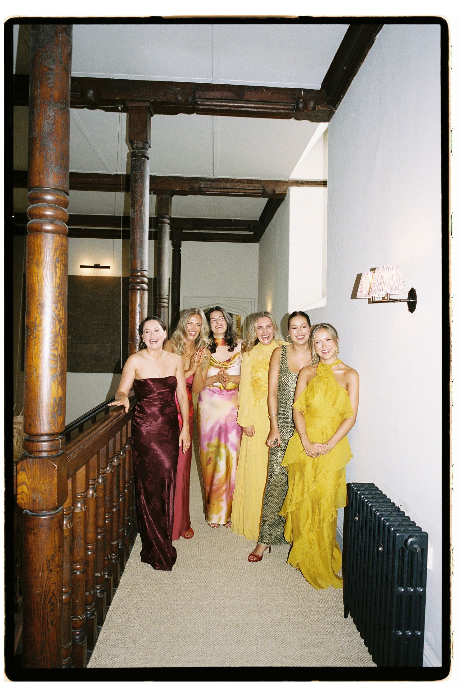 Six women in elegant gowns pose on a staircase at a formal event.