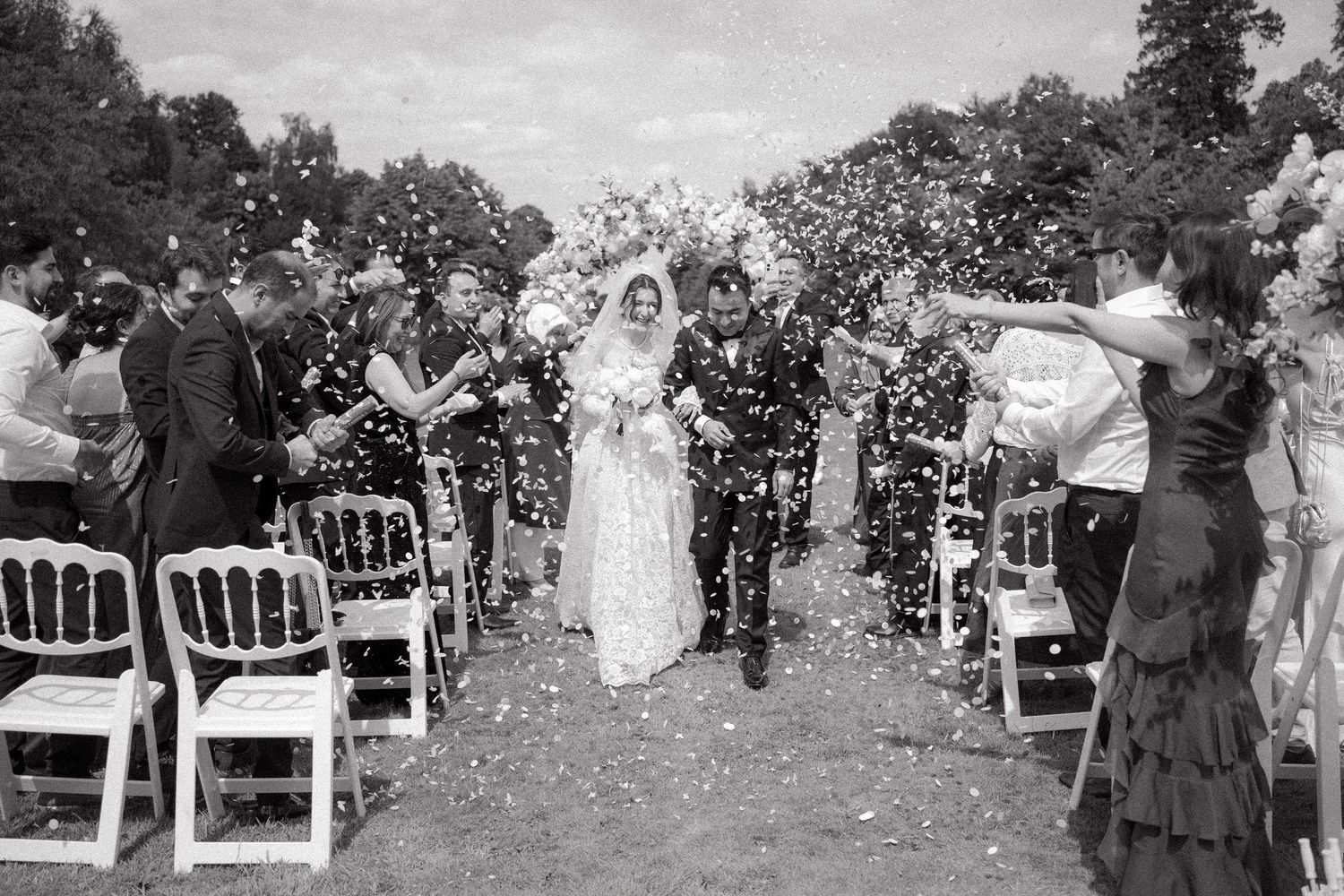 Vintage black and white photograph of a garden wedding ceremony with guests seated in white chairs outdoors.