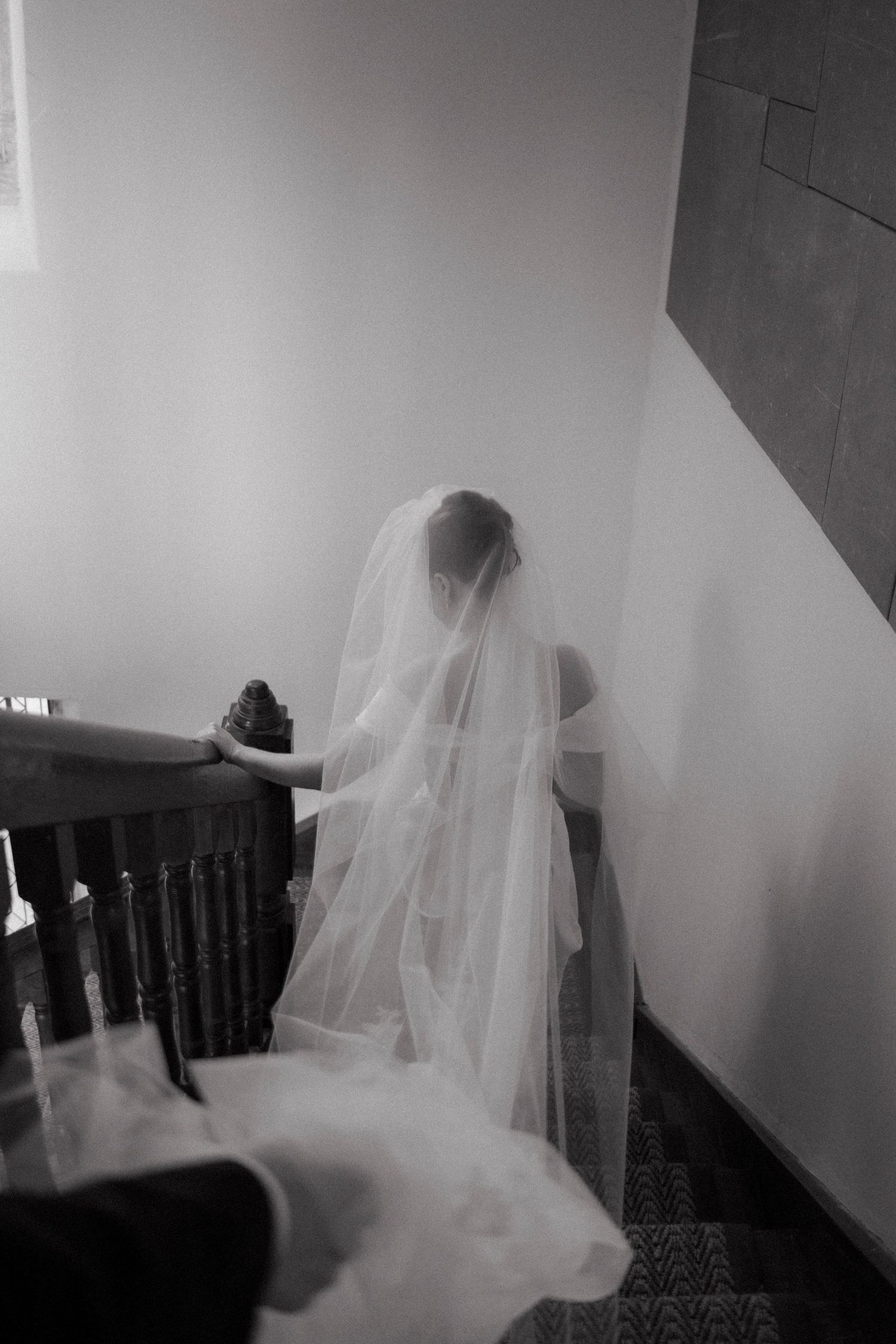 Bride in white wedding gown and long veil descending staircase in black and white wedding photo.