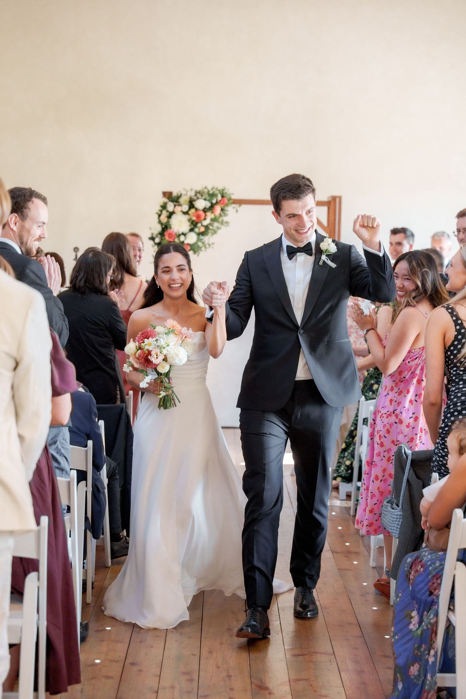 Wedding party members celebrate joyfully while walking down the aisle after the ceremony.