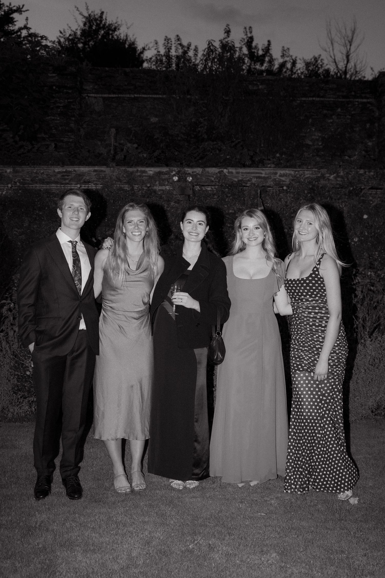 A black and white group photo taken outdoors showing several people standing in a line at dusk.