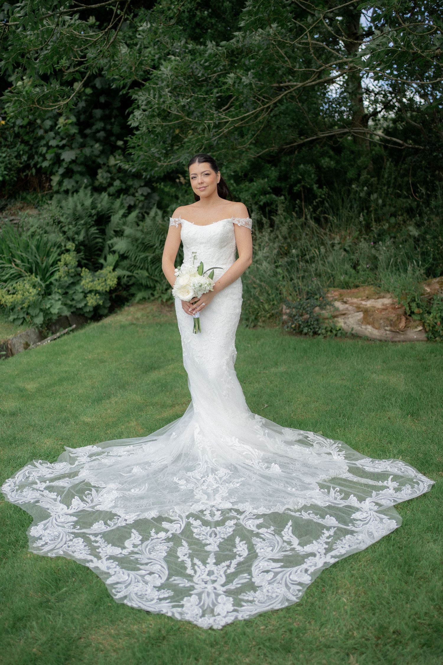 Stunning lace wedding dress with intricate train spread out on green grass.
