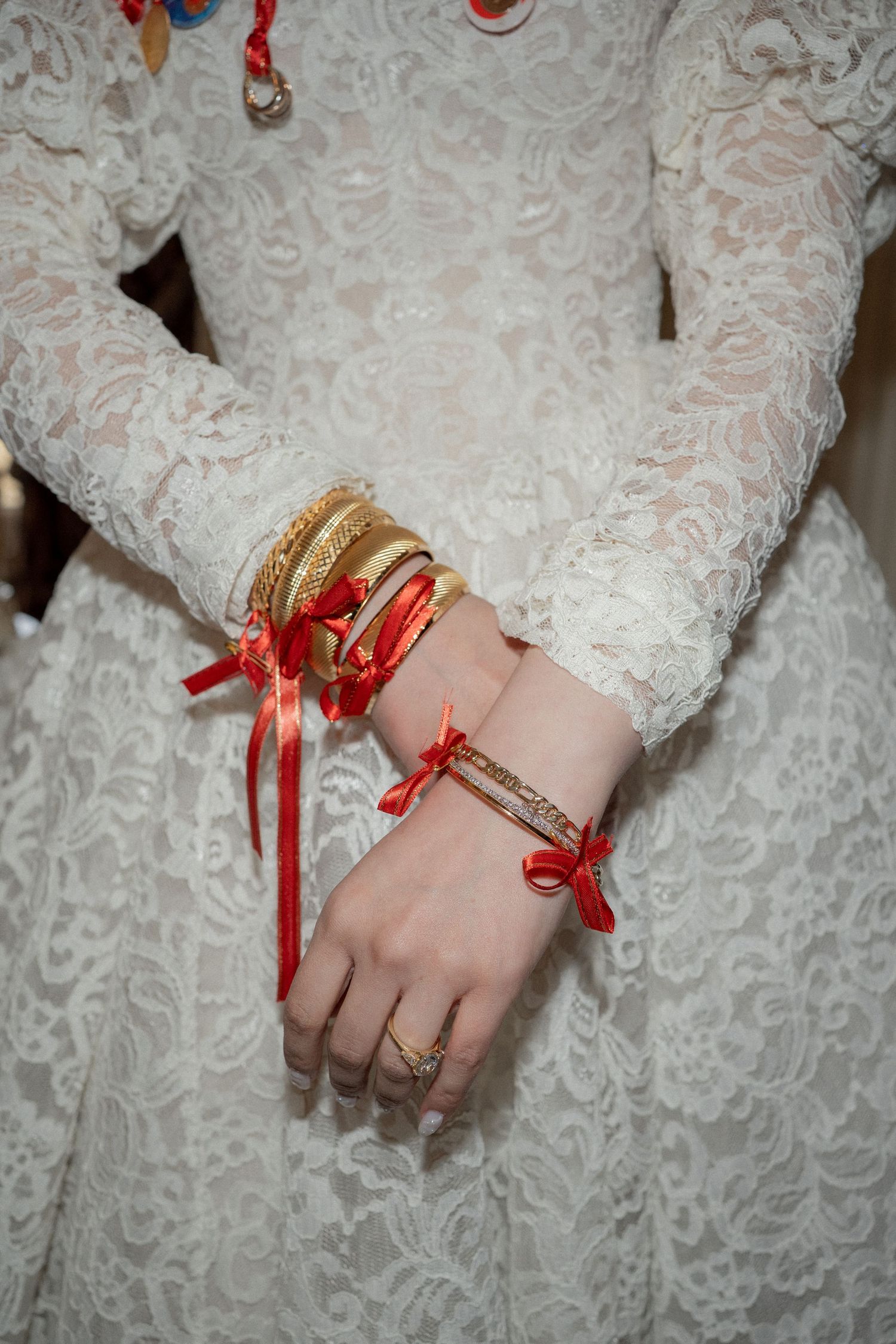 Wedding dress detail showing lace sleeves adorned with red ribbons and gold bangles.
