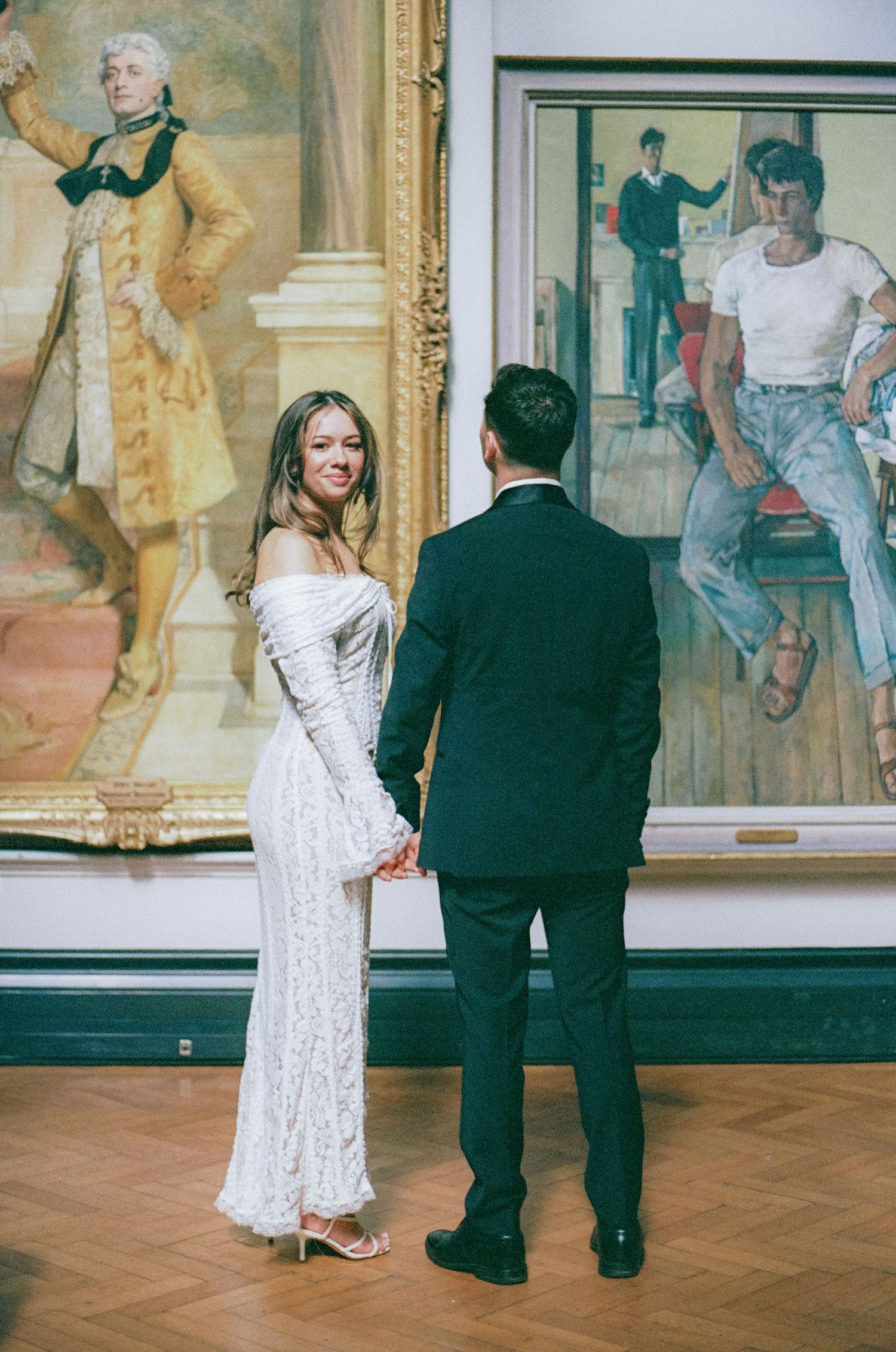Couple in formal wedding attire viewing artwork in an elegant gallery setting.