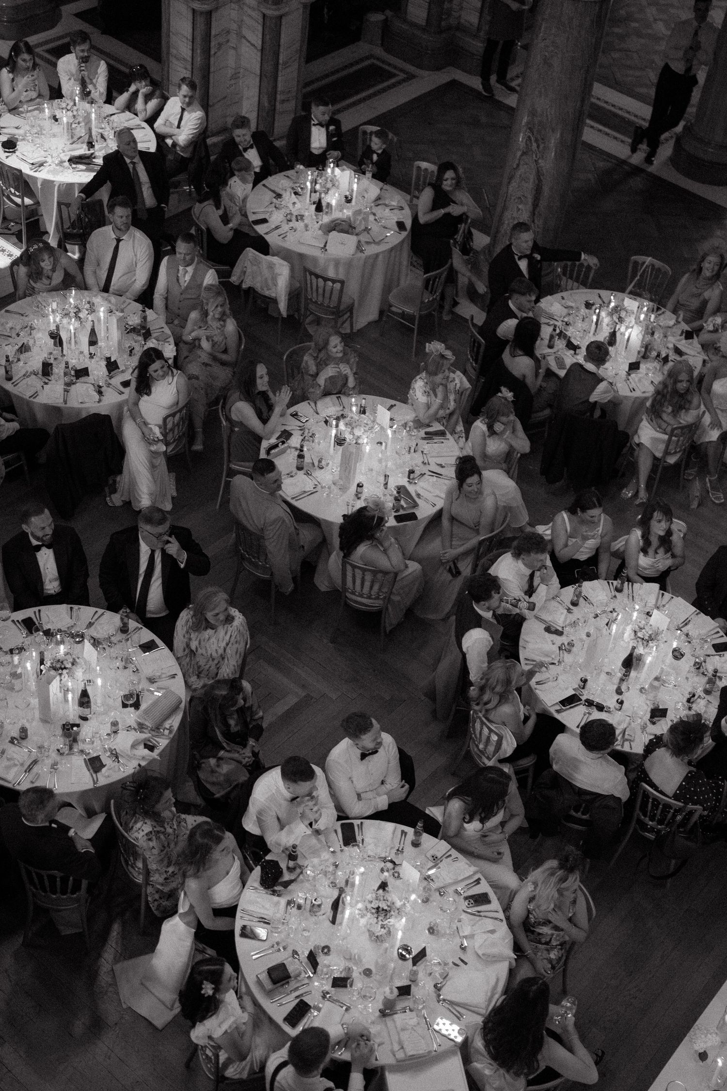Overhead view of a formal dining event with multiple round tables filled with guests in an ornate hall.