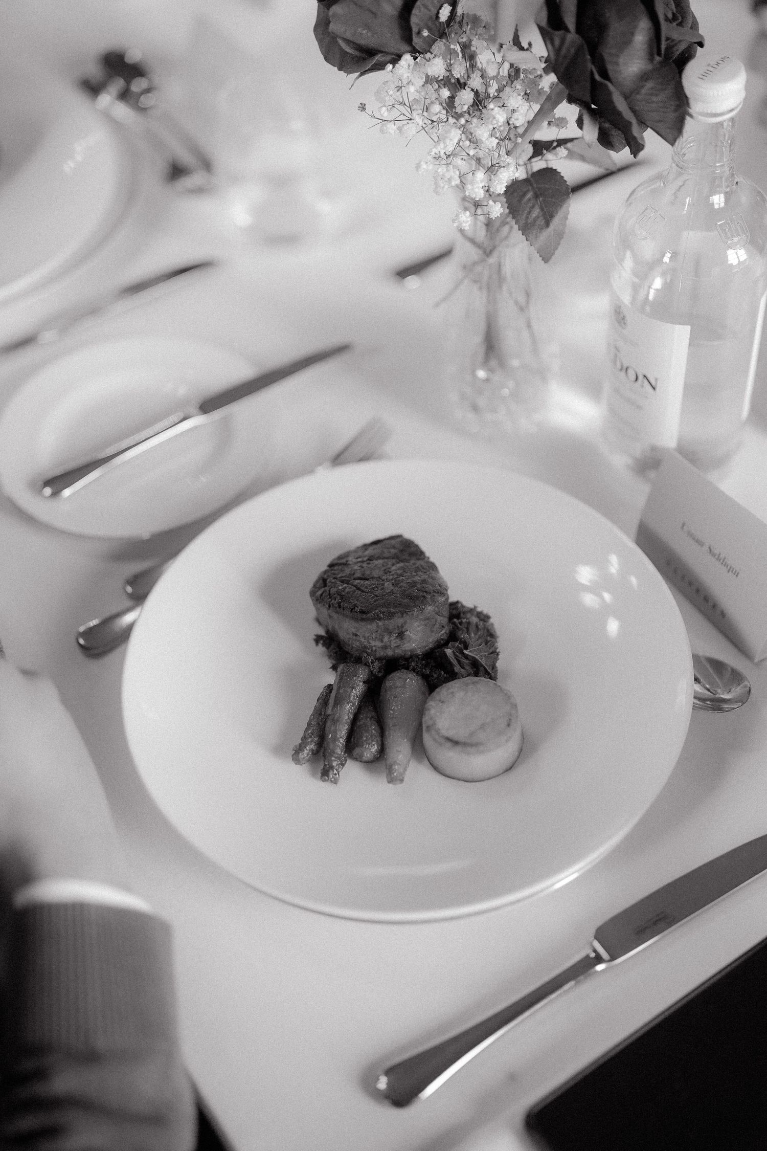 Black and white photo of an elegant plated dinner course with meat and vegetables on a white plate at a formal event.