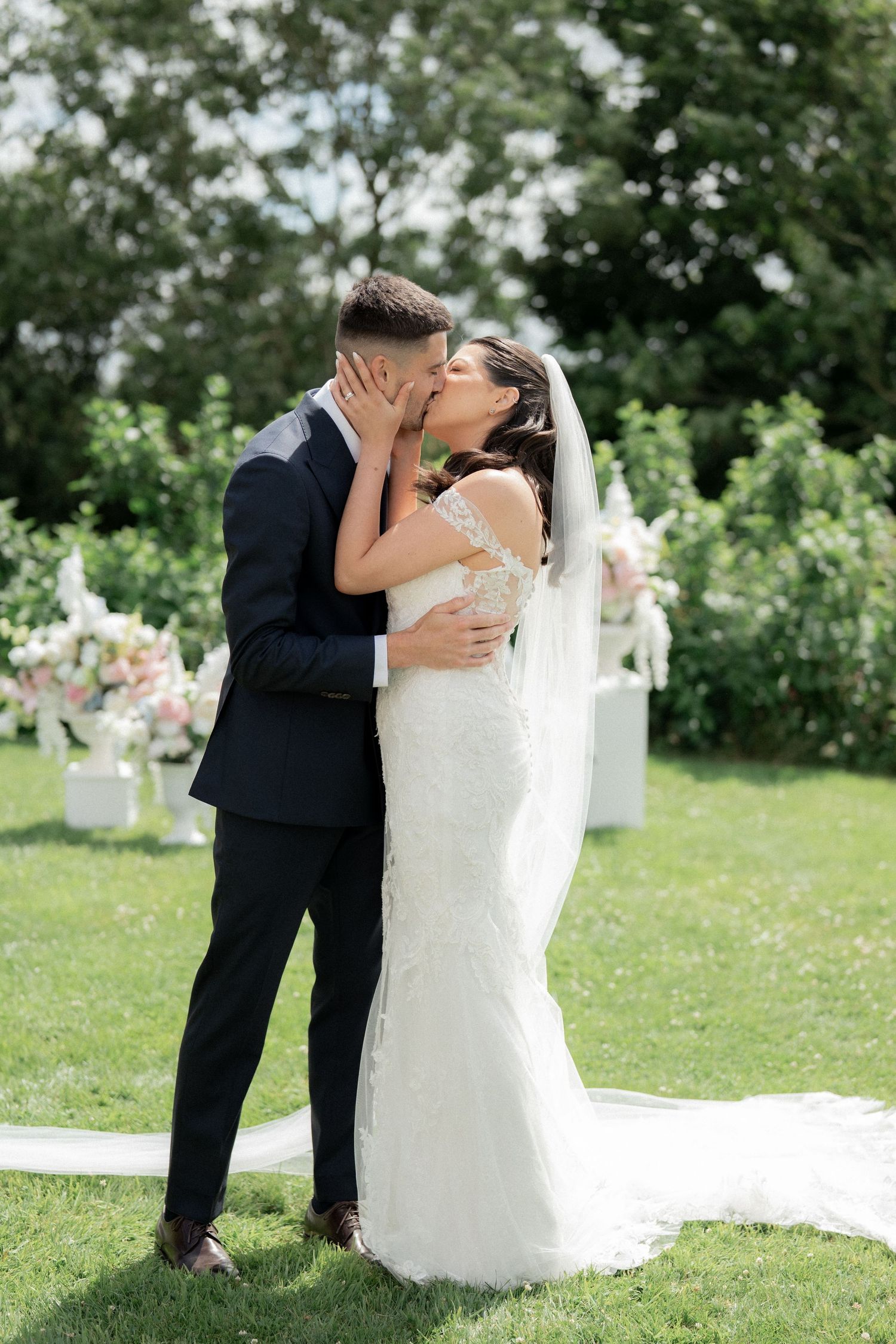 Romantic wedding moment captured in a sunlit garden with white floral decorations.