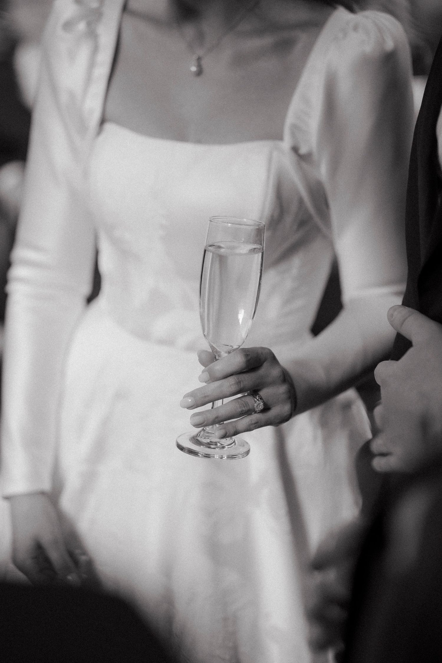Bride in white gown holding champagne flute with wedding ring visible at reception.