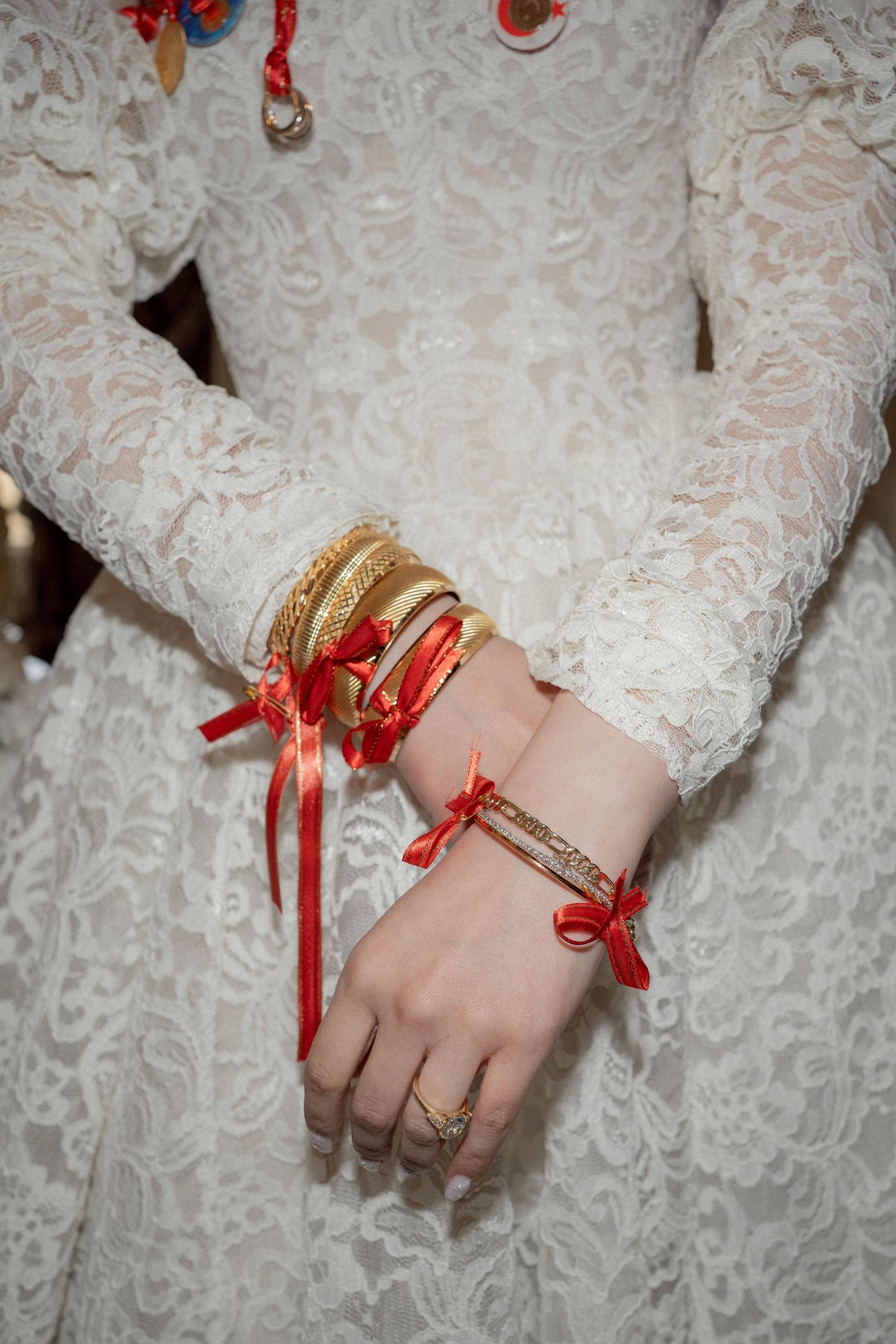 Close-up of hands wearing lace sleeves adorned with gold bangles and red ribbons tied around the wrist.