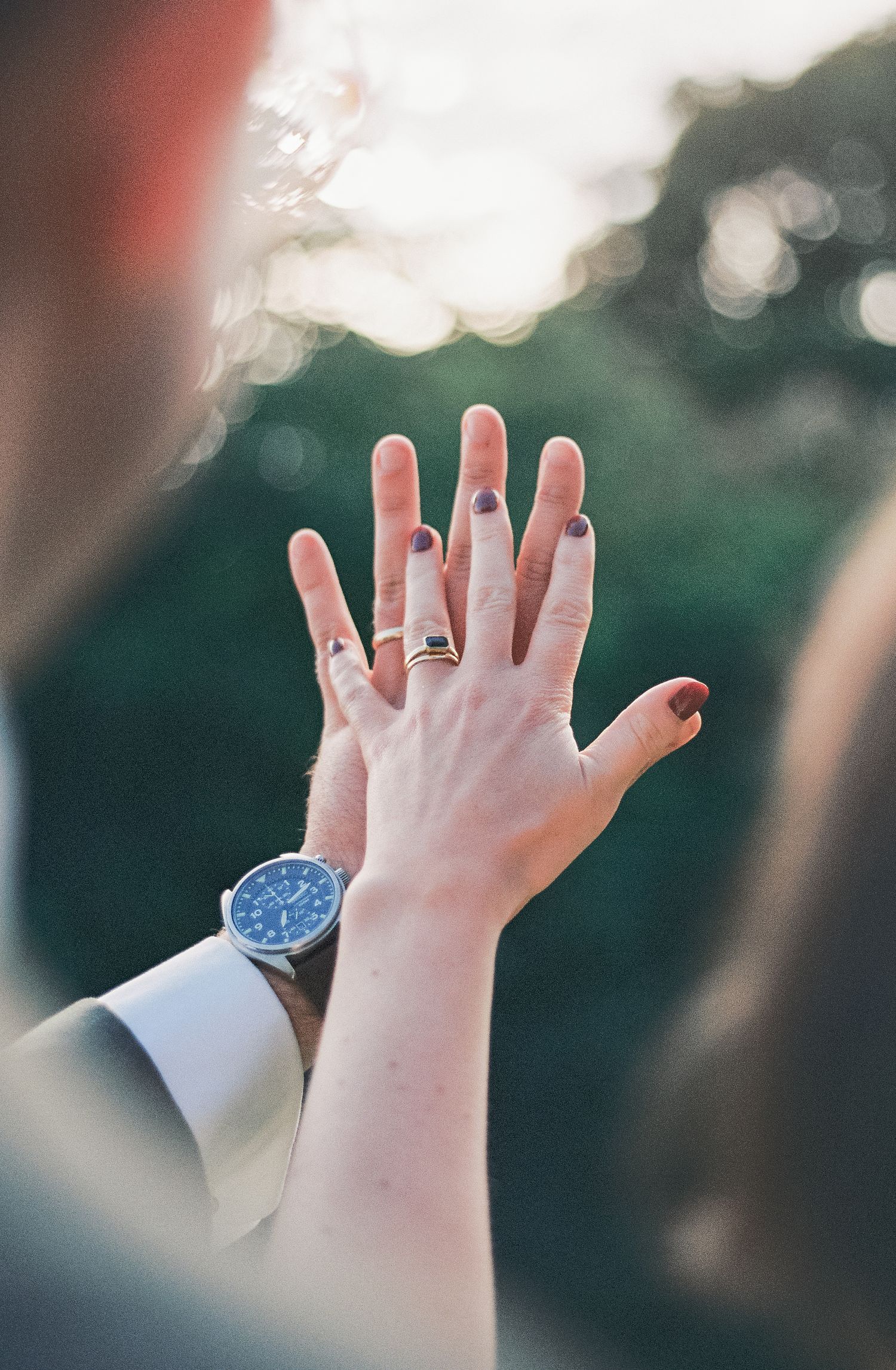 Close-up of hands showing wedding rings against a blurred natural background.