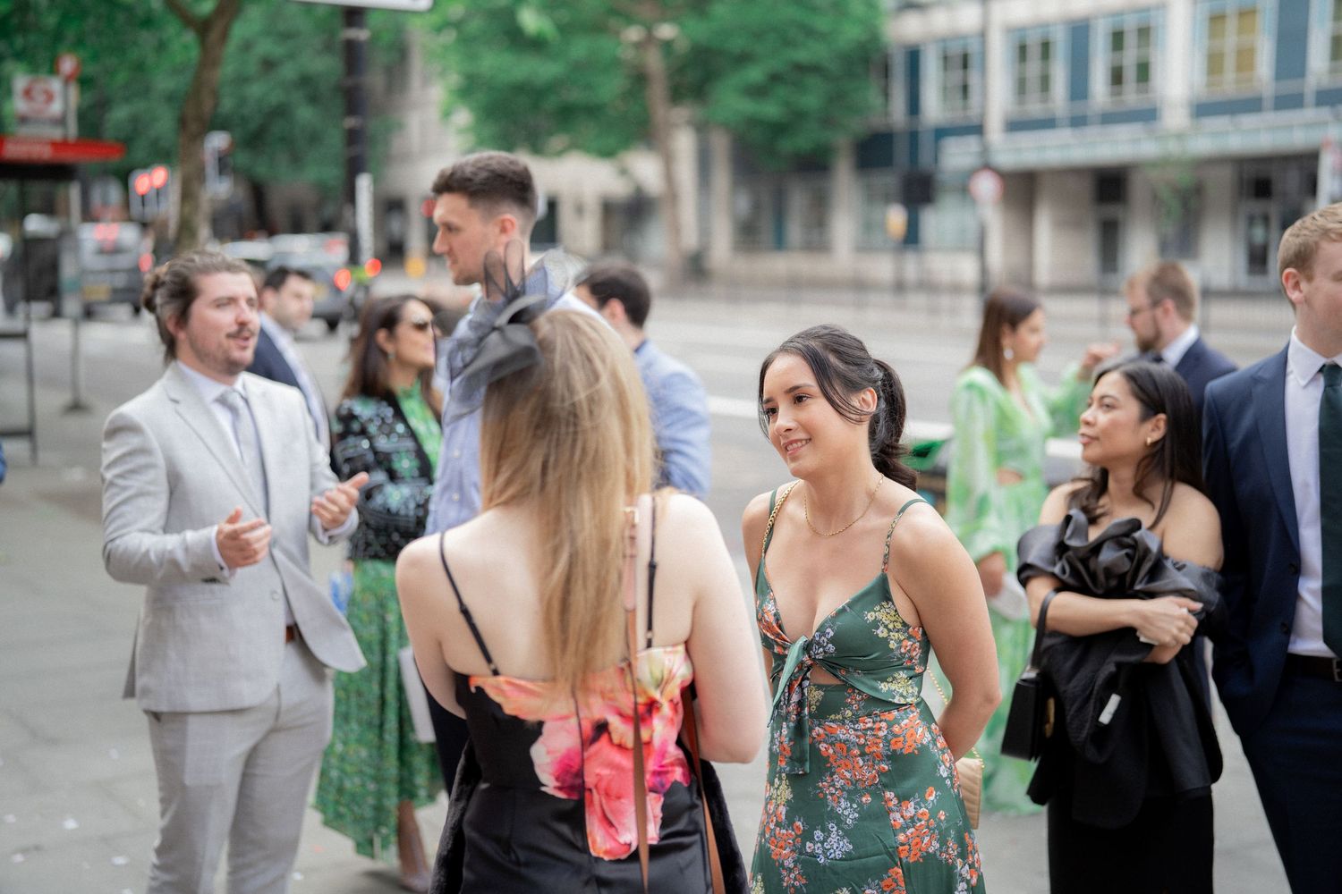 Wedding guests mingling outdoors in formal attire with greenery in the background.