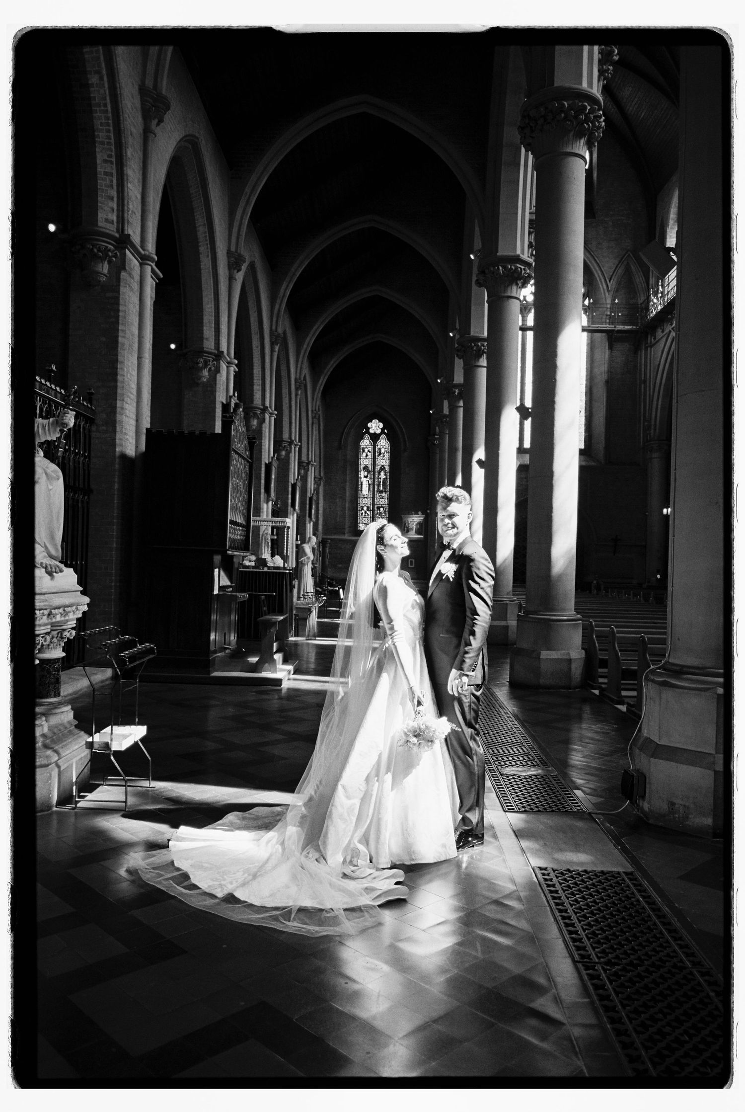 Dramatic black and white photo of bride and groom embracing inside historic Gothic church with arched columns.