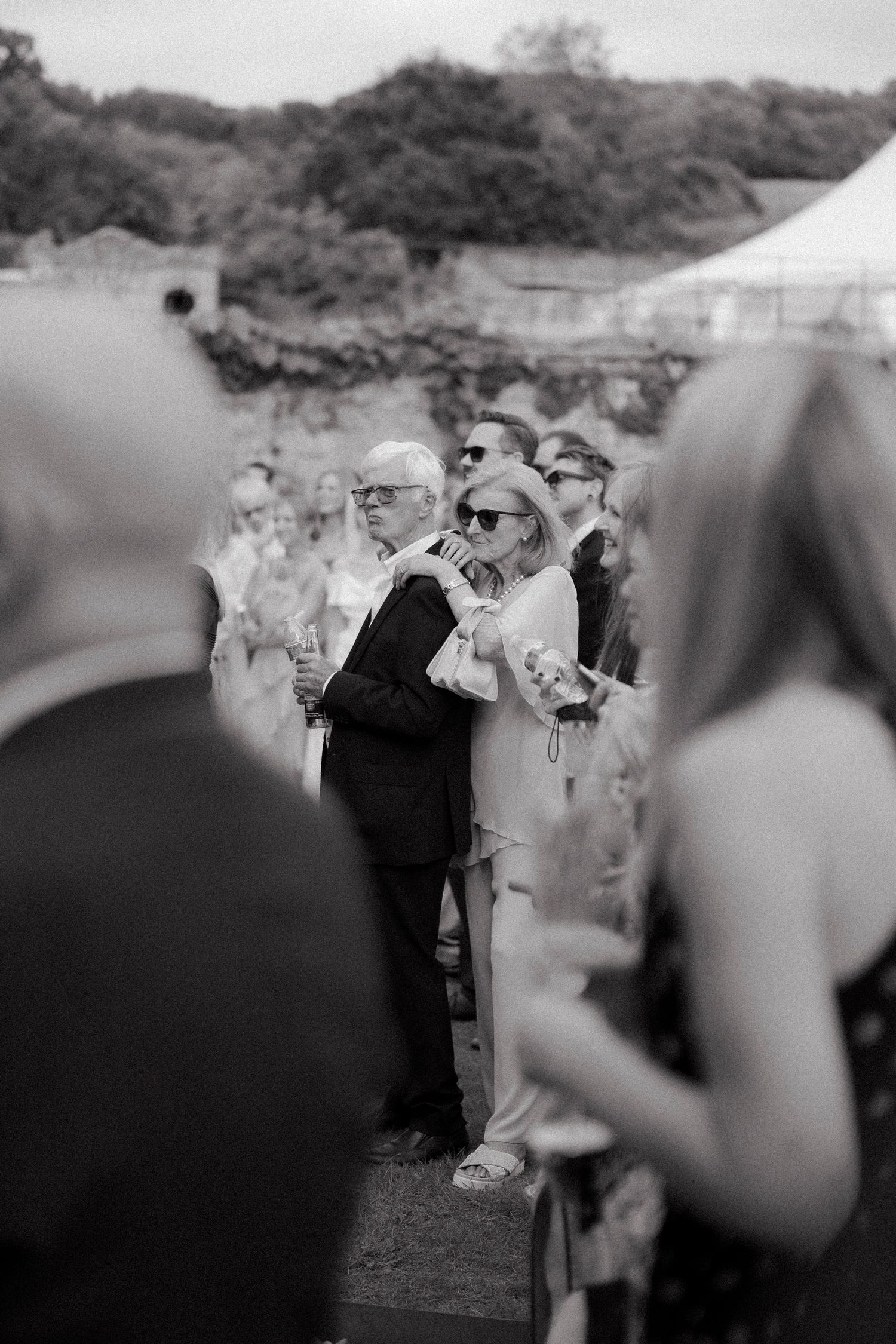 Black and white wedding photo of elegantly dressed guests mingling outdoors at a garden ceremony.