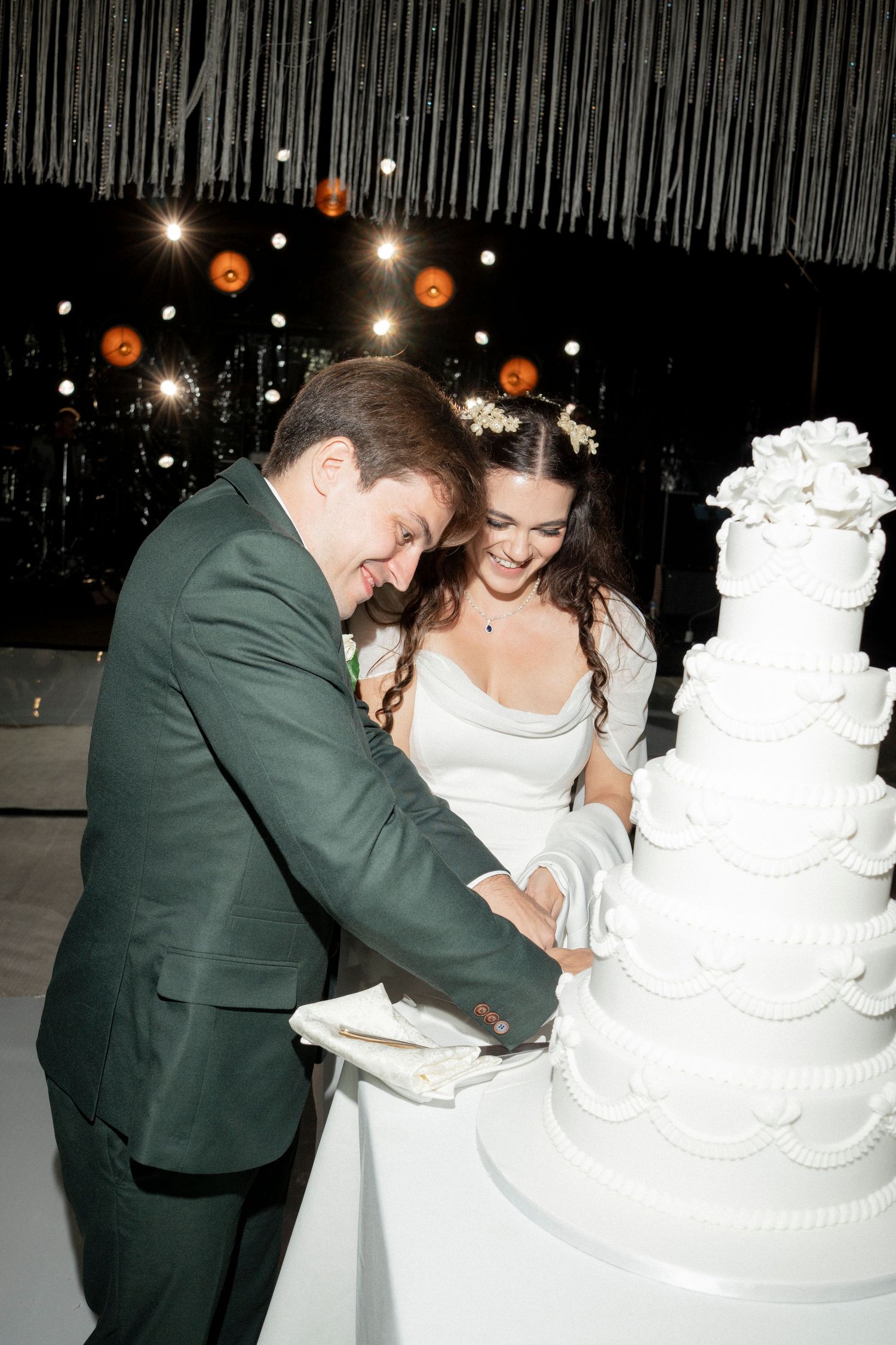 Bride and groom cutting a tall white tiered wedding cake together at their reception.
