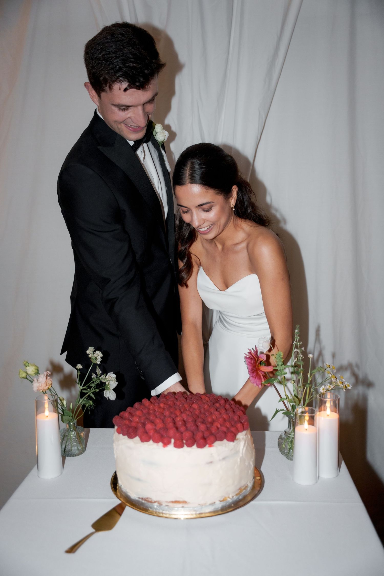 A couple cuts their white wedding cake decorated with red raspberries at their reception.