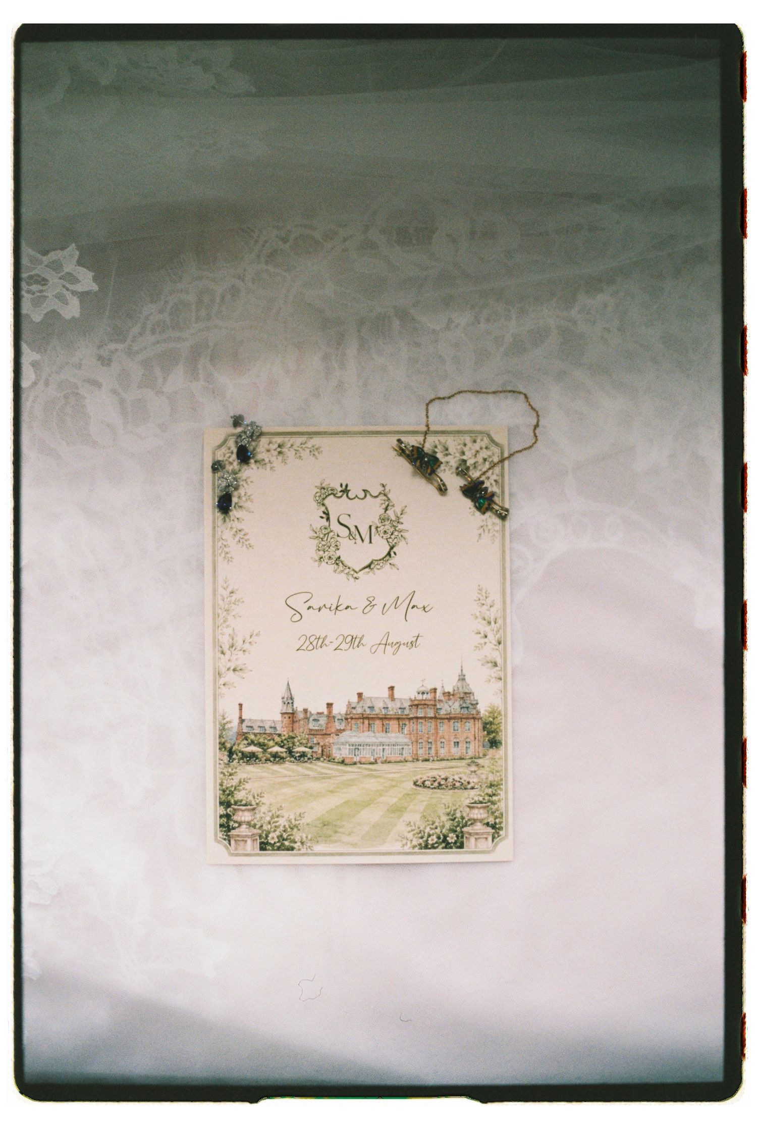 Elegant wedding invitation featuring a watercolor illustration of a manor house with floral details and couple's monogram.