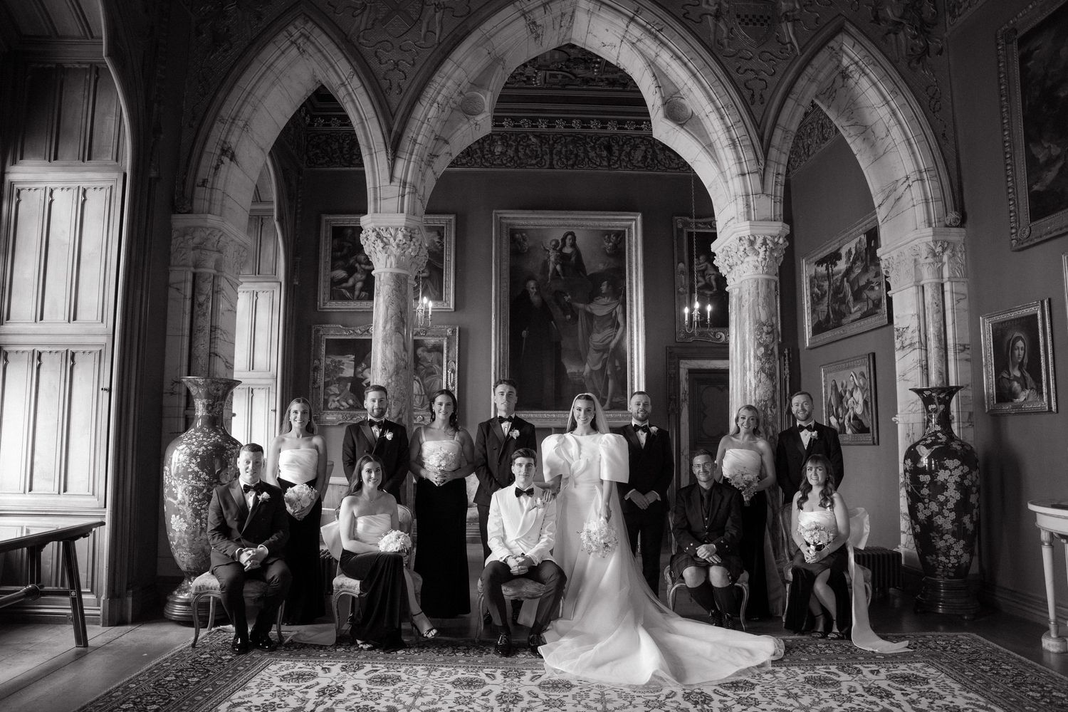 Elegant wedding party poses in ornate cathedral interior with gothic arches and dramatic lighting.