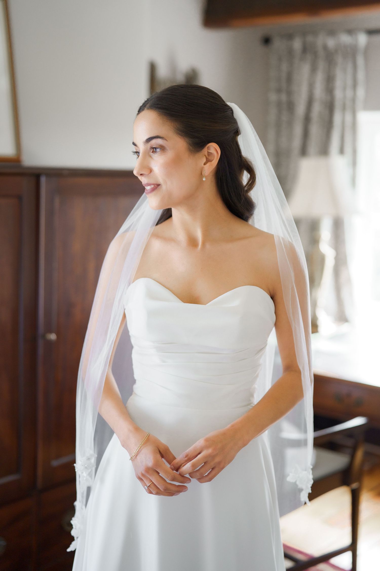 A bride in a classic white strapless wedding dress poses elegantly in an indoor setting.