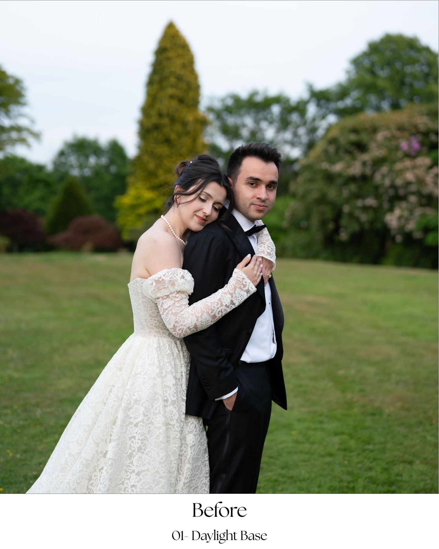 A couple in formal wedding attire embraces on a green lawn with trees in the background.
