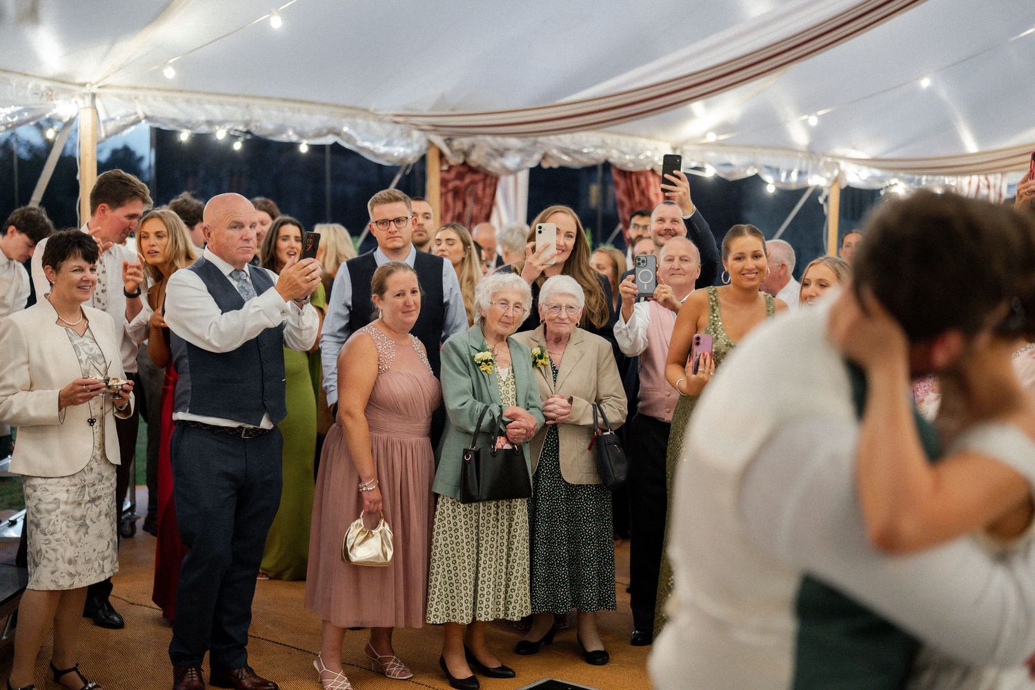 Wedding guests watch emotional first dance of newlyweds in a decorated marquee venue.
