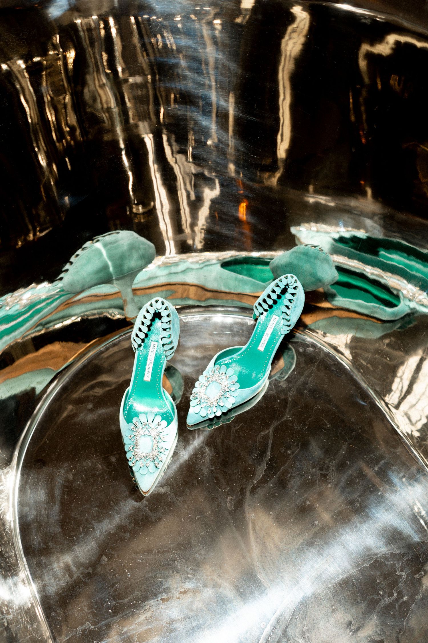 Teal embellished bridal heels with crystal flower detail placed inside a metallic silver bathtub.