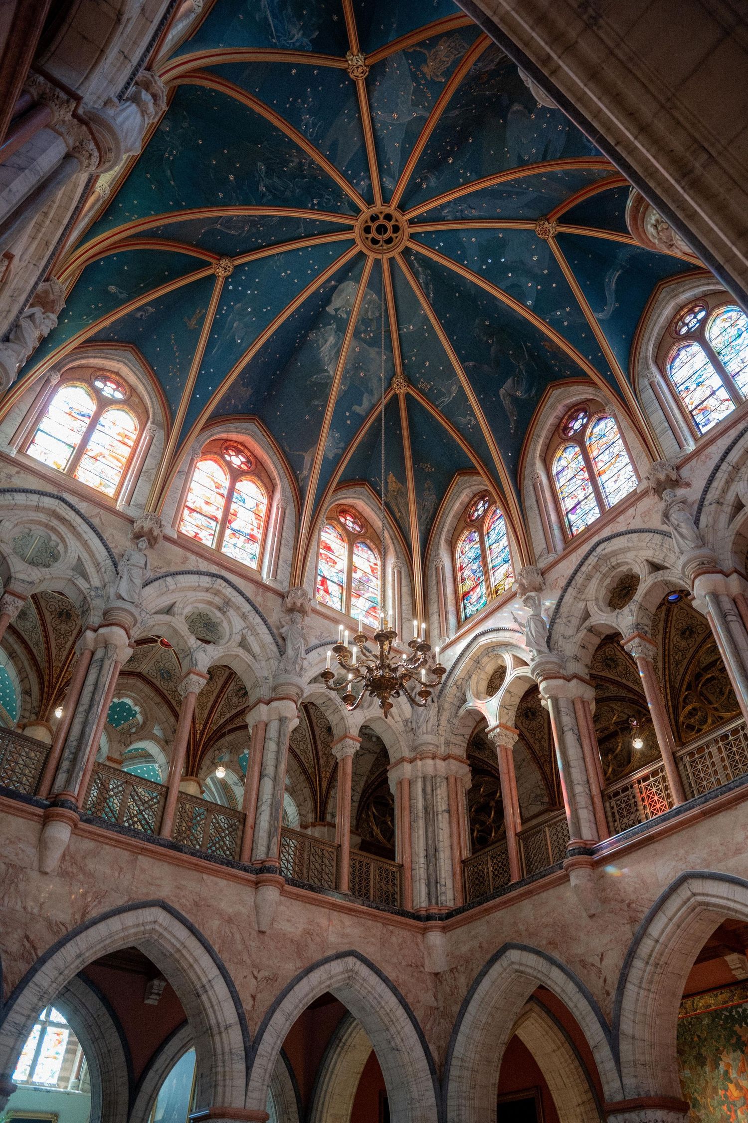Ornate cathedral ceiling with blue vaulted arches, stained glass windows, and decorative architectural details.