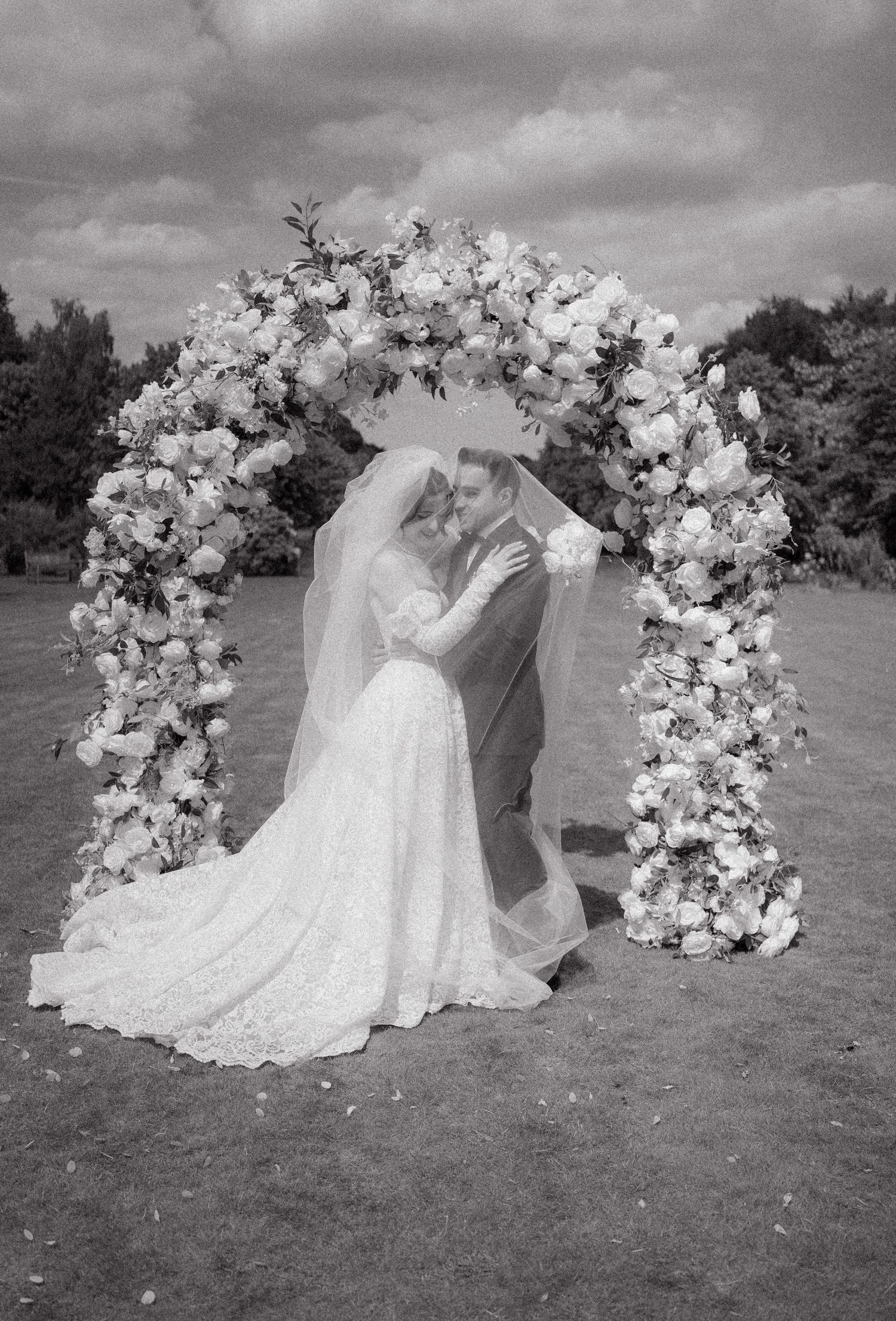 Outdoor wedding arch decorated with white floral arrangements against a cloudy sky.