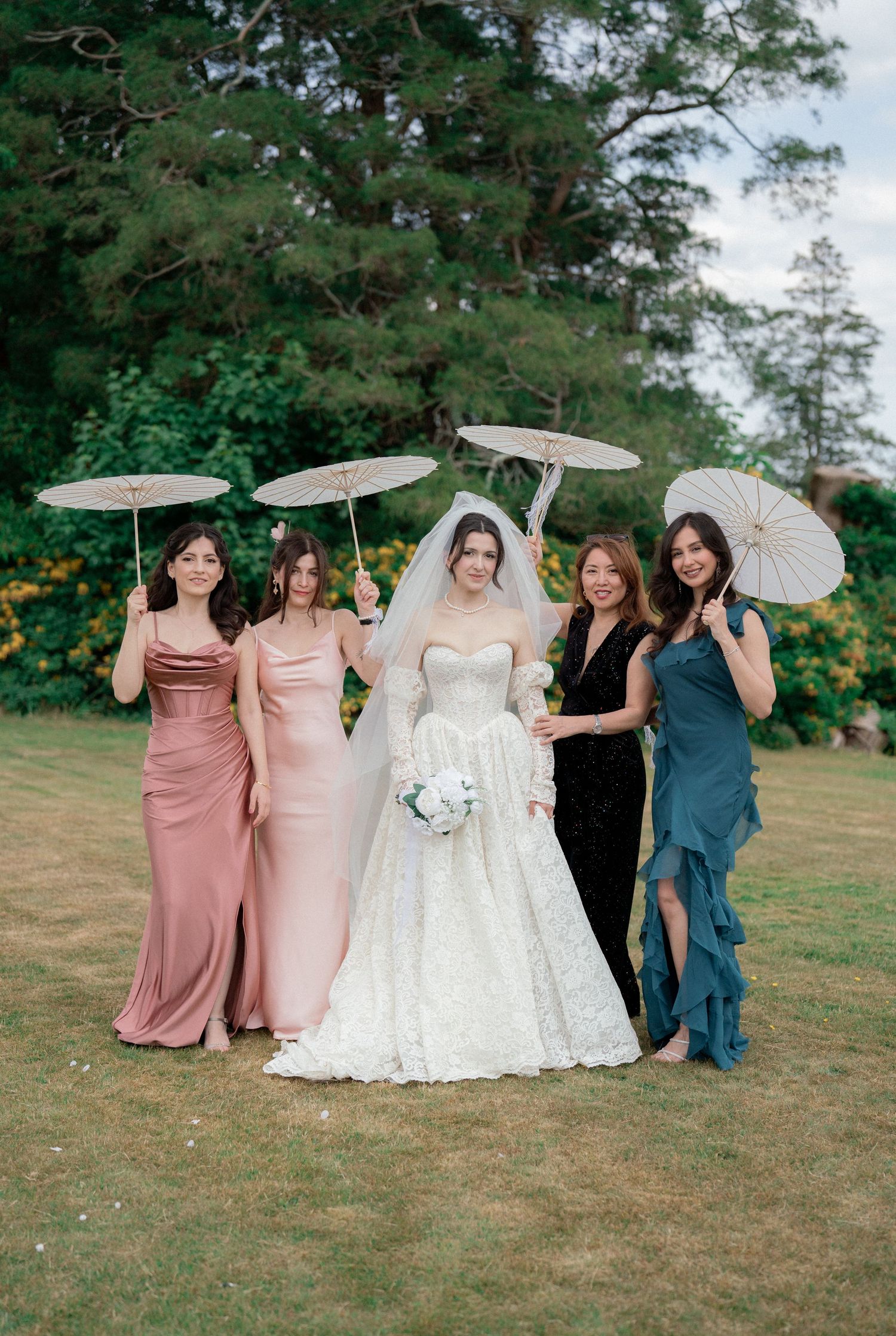 Wedding party with parasols poses on grassy hill wearing pink and navy dresses.