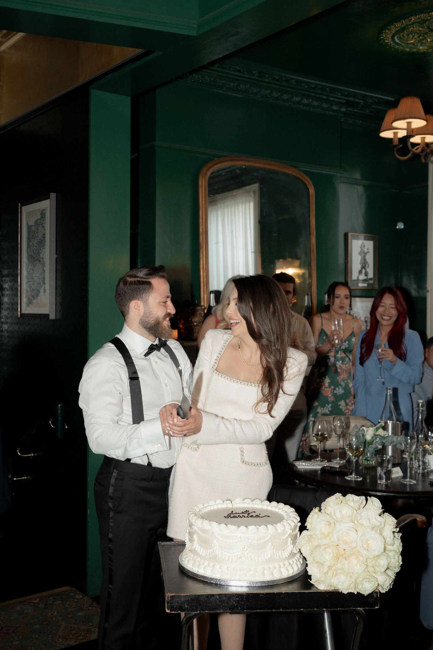 Wedding reception scene in a dark green room with cake display and floral arrangements.