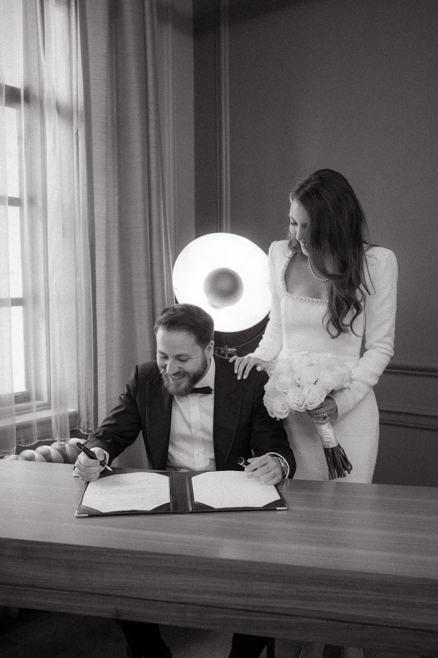 Two people in formal wear sign documents at a wooden table.