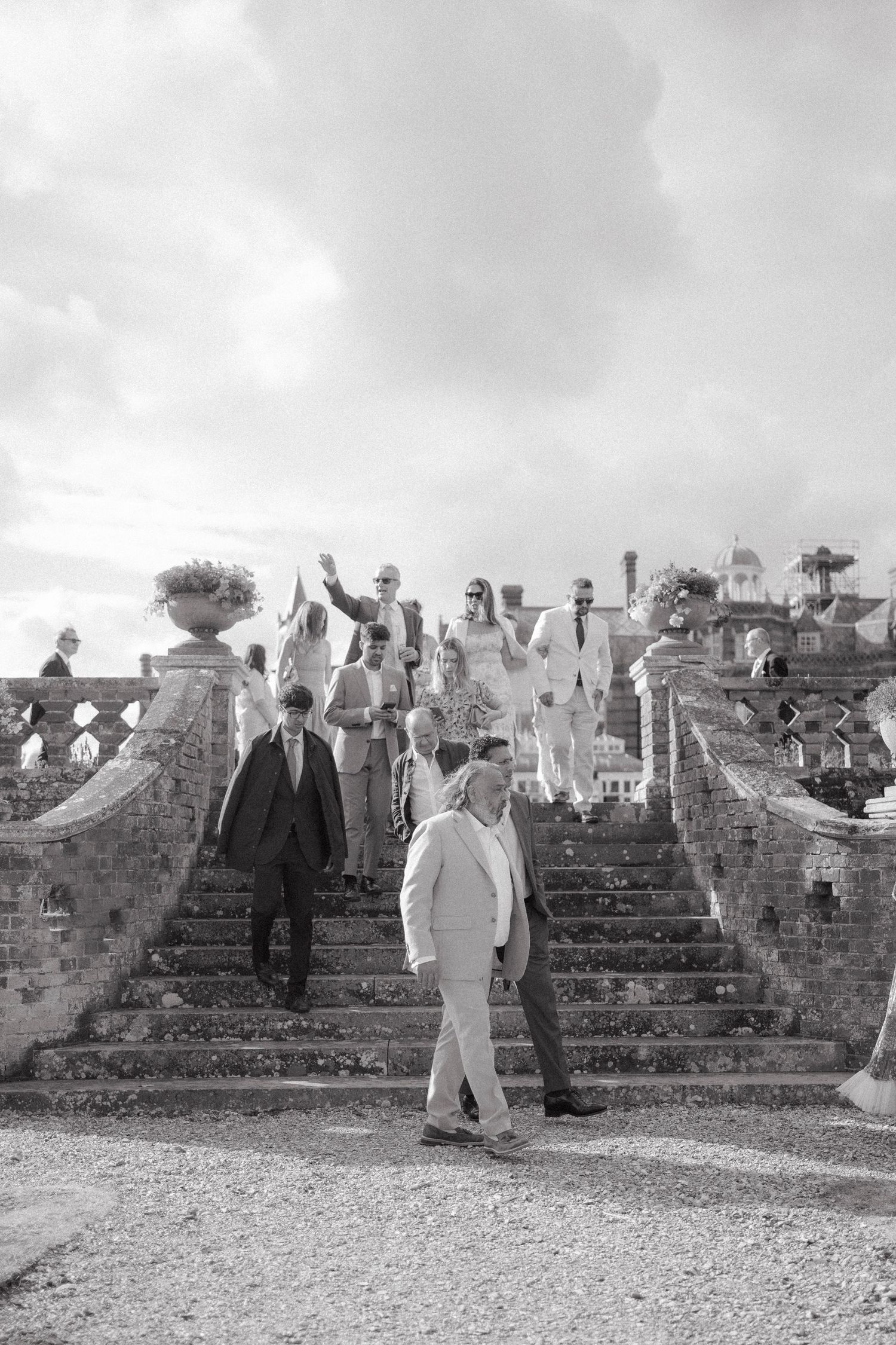 Black and white photo of wedding guests descending ornate stone stairs at an elegant outdoor venue.