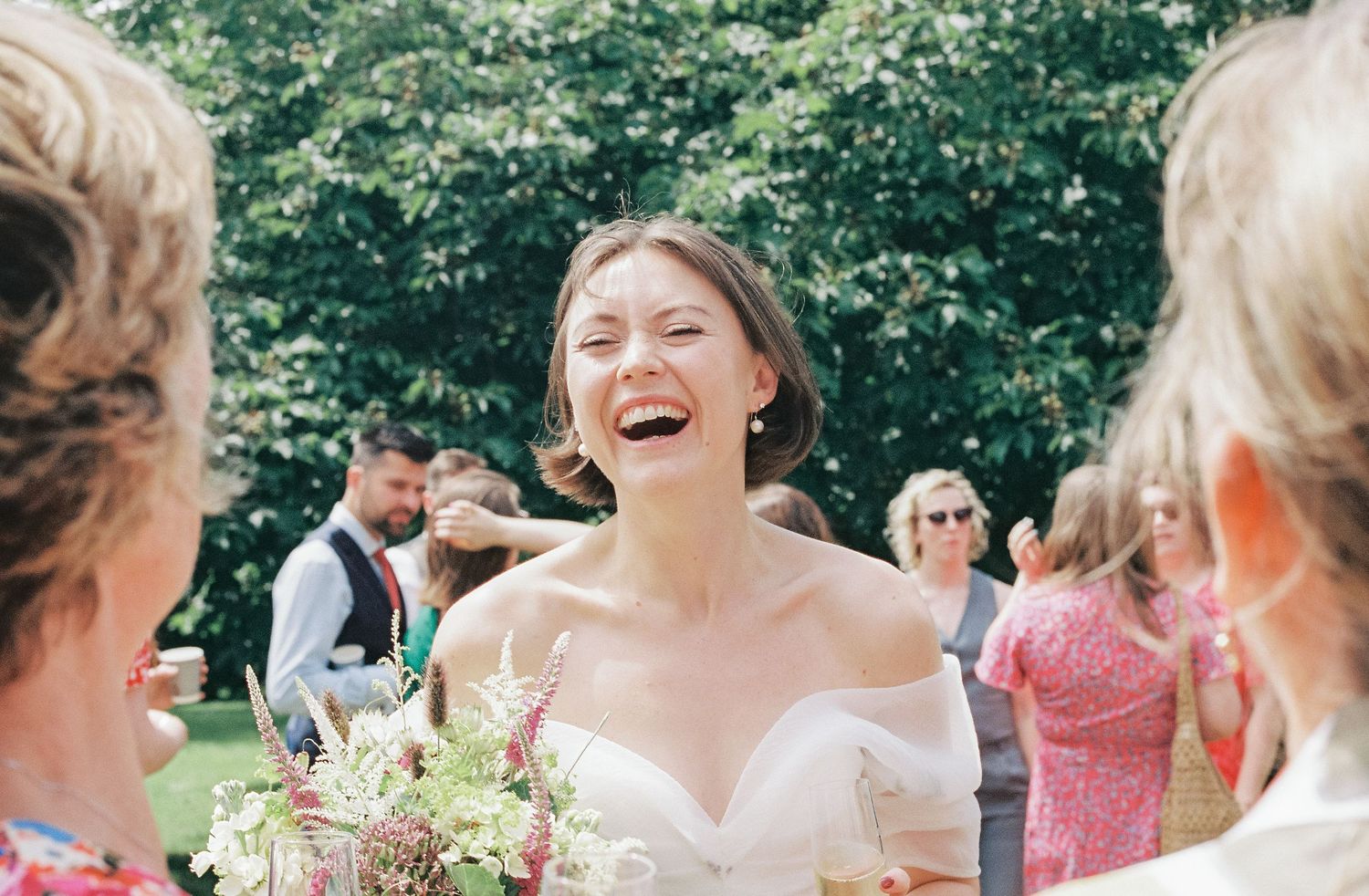 Wedding guests share joyful laughter during an outdoor celebration.