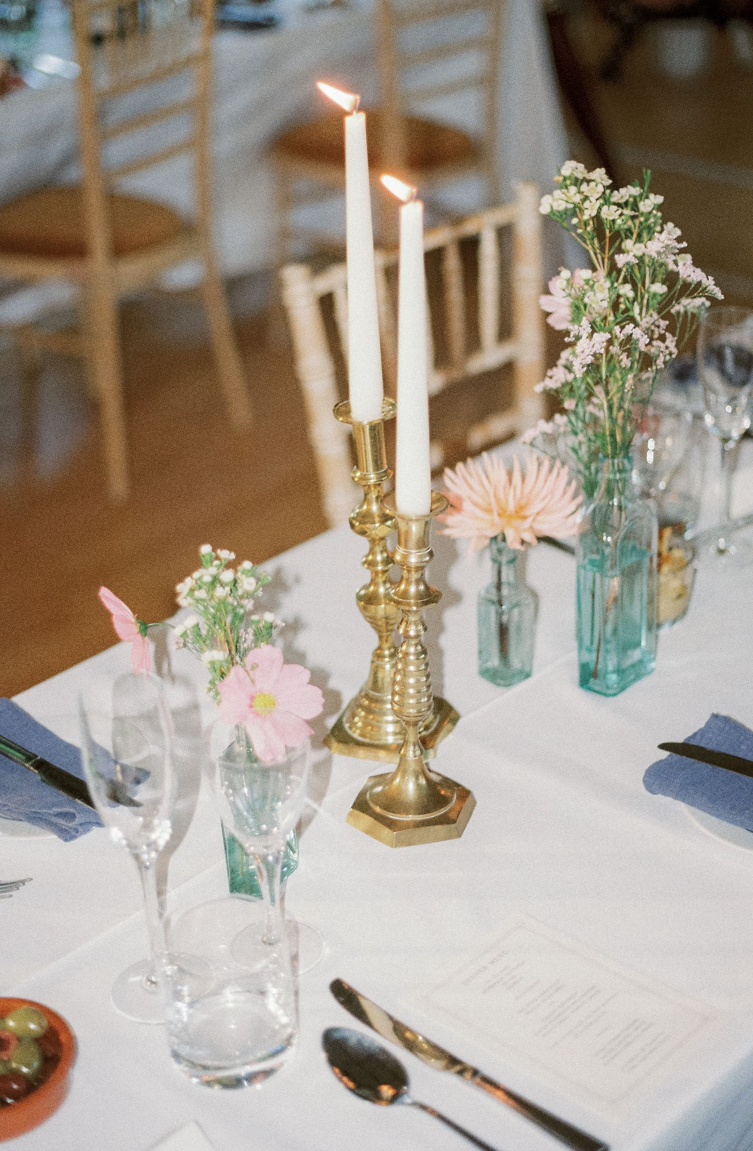 Elegant table settings with blue mason jars, pink flowers, and gold candlesticks create a romantic wedding reception atmosphere.