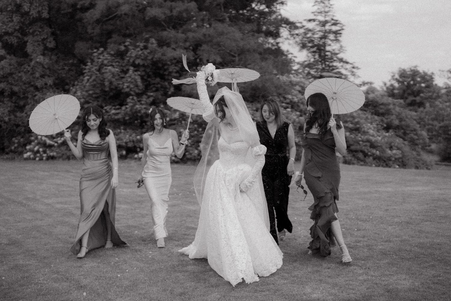 Black and white photo of wedding guests walking across a grassy outdoor venue.