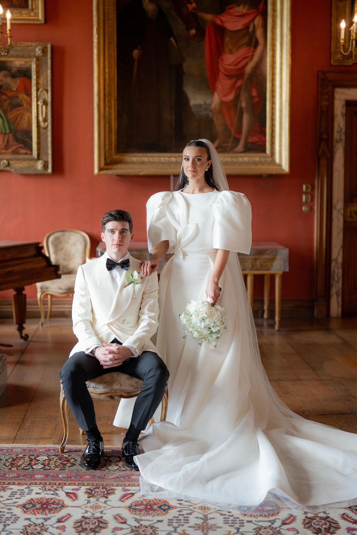 Wedding portrait session in an elegant red room with ornate gold-framed paintings.
