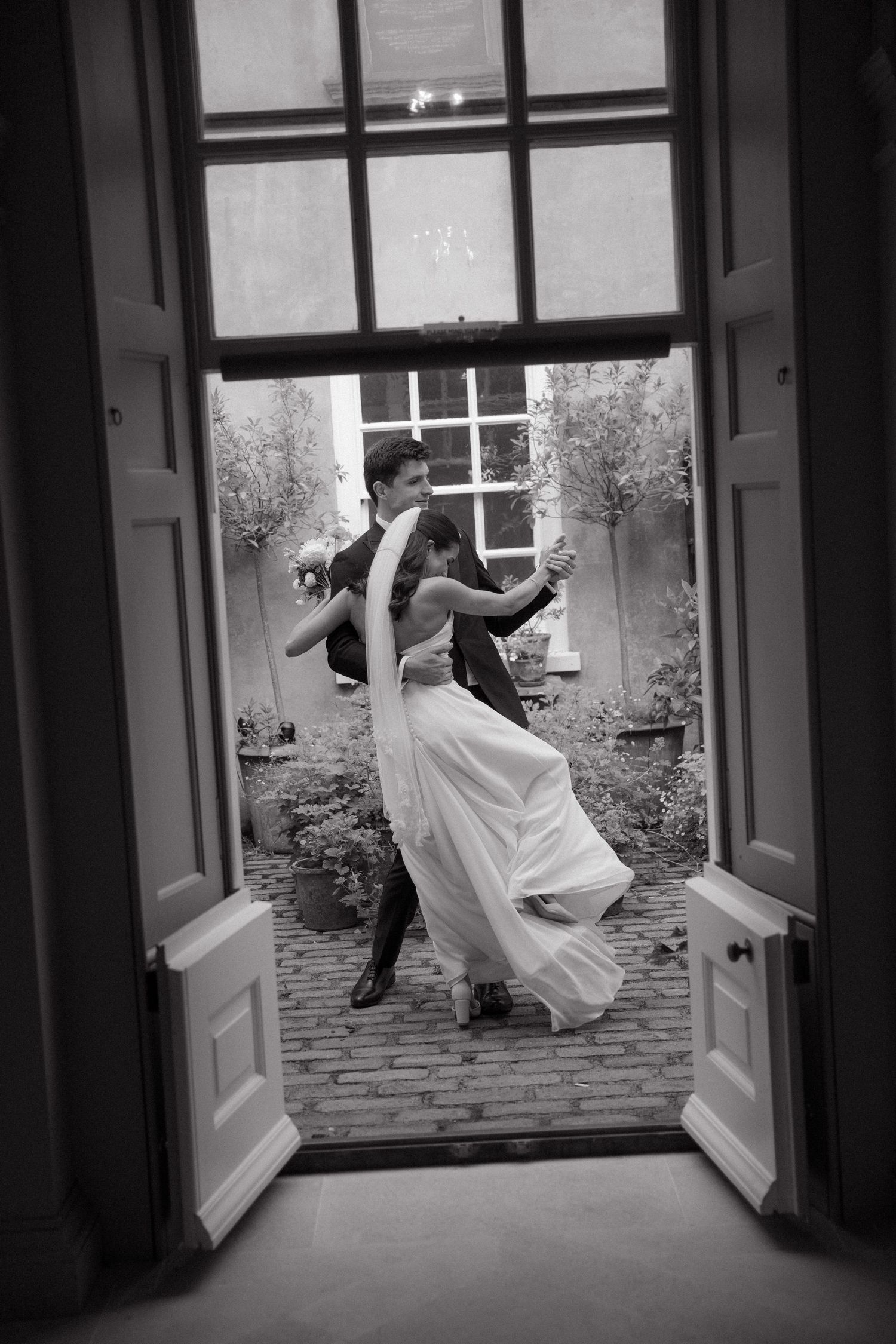 A sequence of black and white photos showing a couple dancing through a doorway in elegant wedding attire.