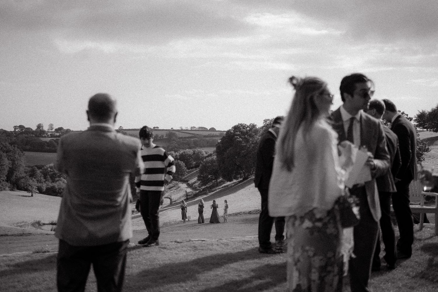 Black and white photograph showing silhouettes of people gathered outdoors against a cloudy sky.