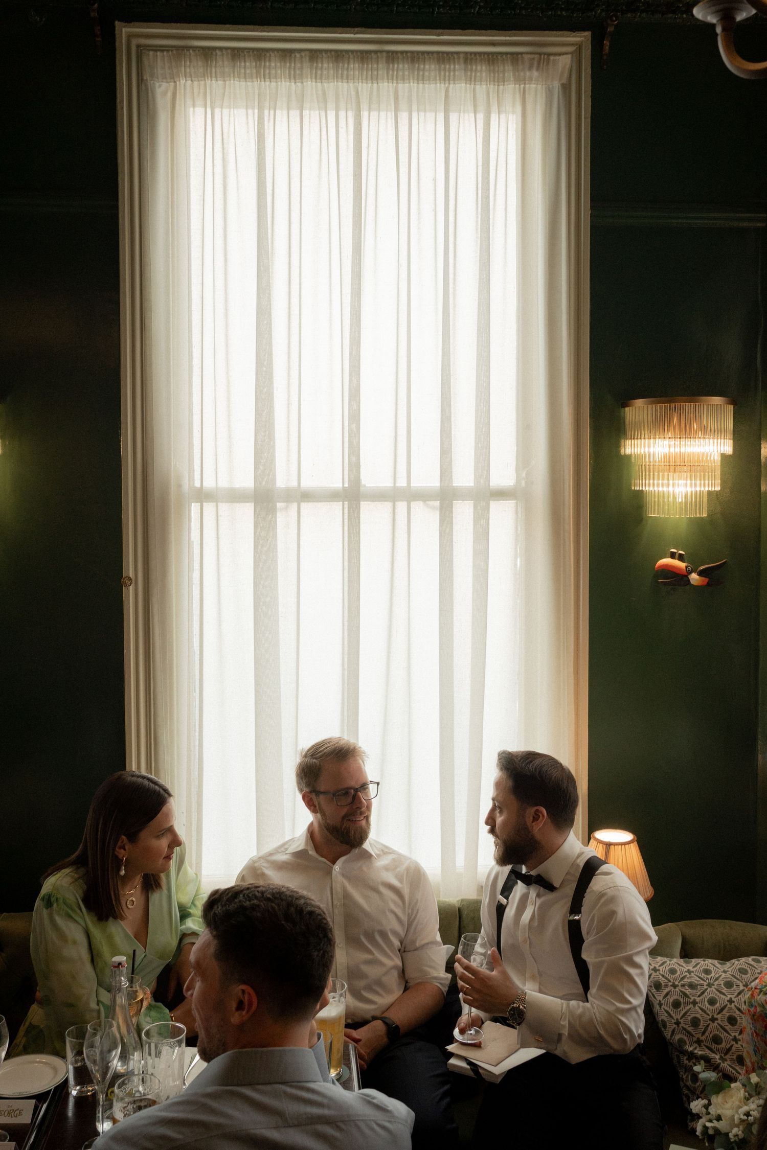 A series of five window-lit photos showing people seated and conversing in an elegant room with dark green walls.